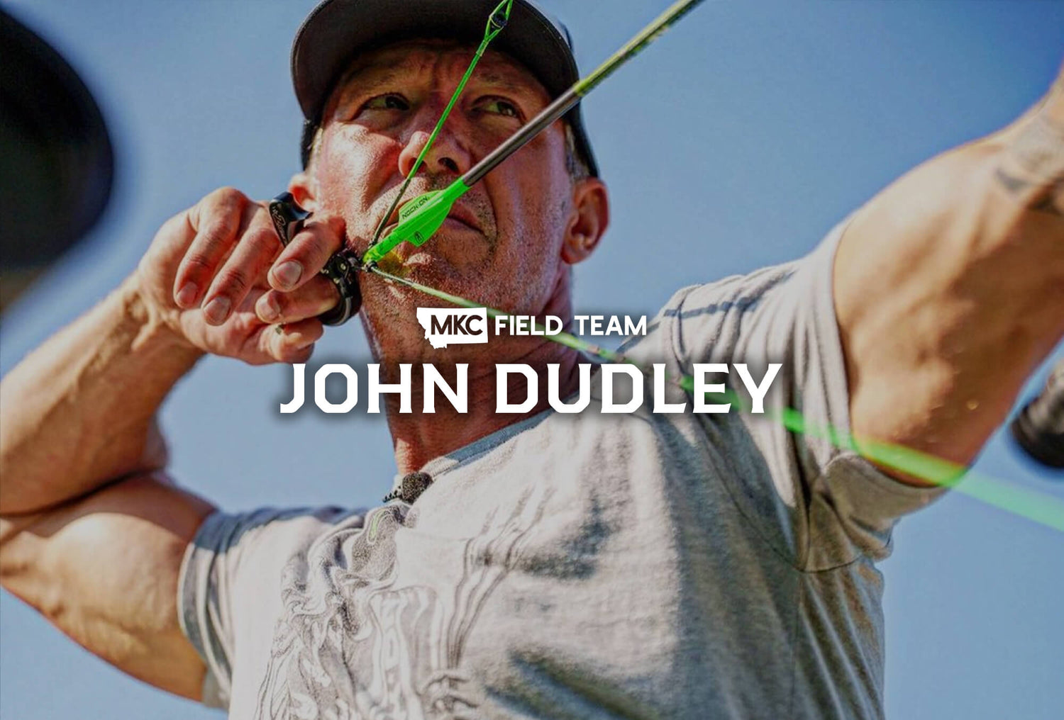 John Dudley stands looking intensely into the distance with an arrow nocked and bow drawn, ready to shoot.