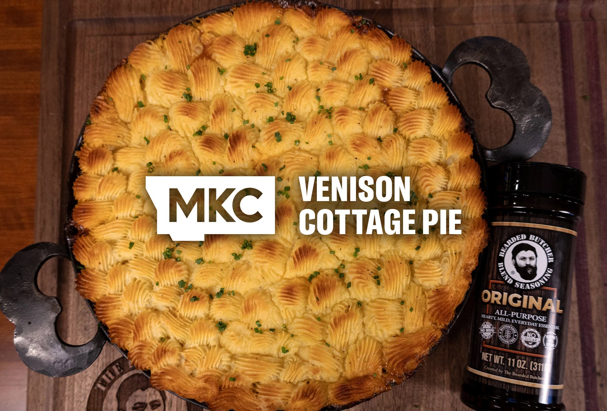 Golden venison cottage pie topped with browned mashed potatoes beside a Bearded Butcher seasoning jar.