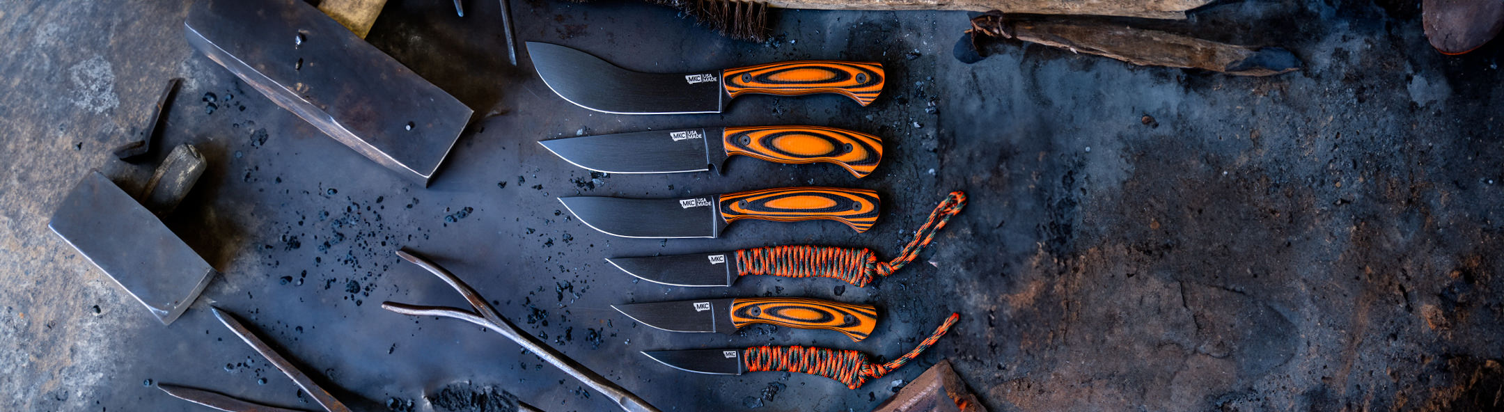 A collection of Montana Knife Company blades featuring various fixed-blade knives with orange and black handles on a textured surface.