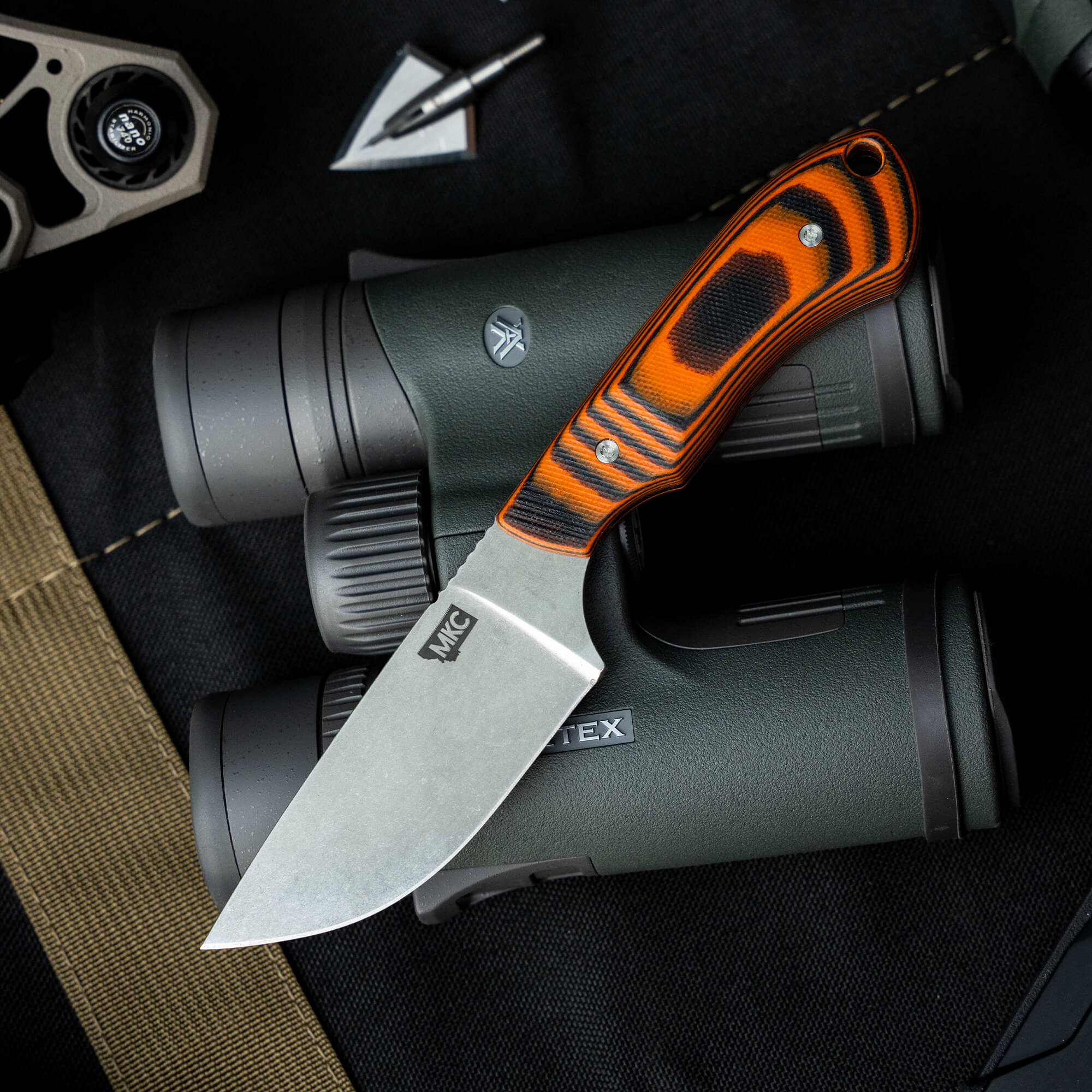 SOLD OUT MKC Elk Knife with a striking orange and black handle, resting on binoculars, showcasing its rugged design.