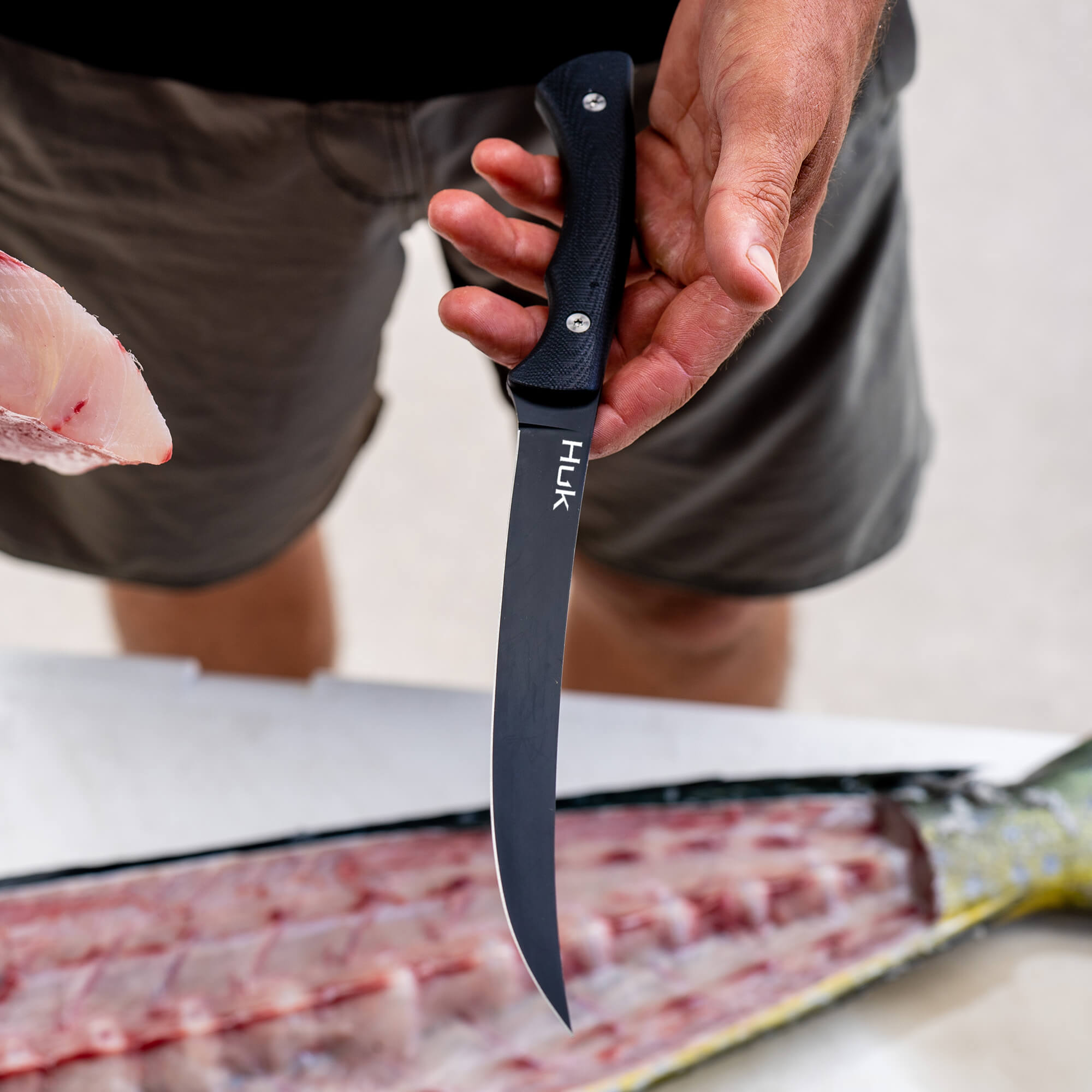 HUK Flathead Fillet knife held by a person, showcasing its curved blade and ergonomic handle, ideal for filleting fish.