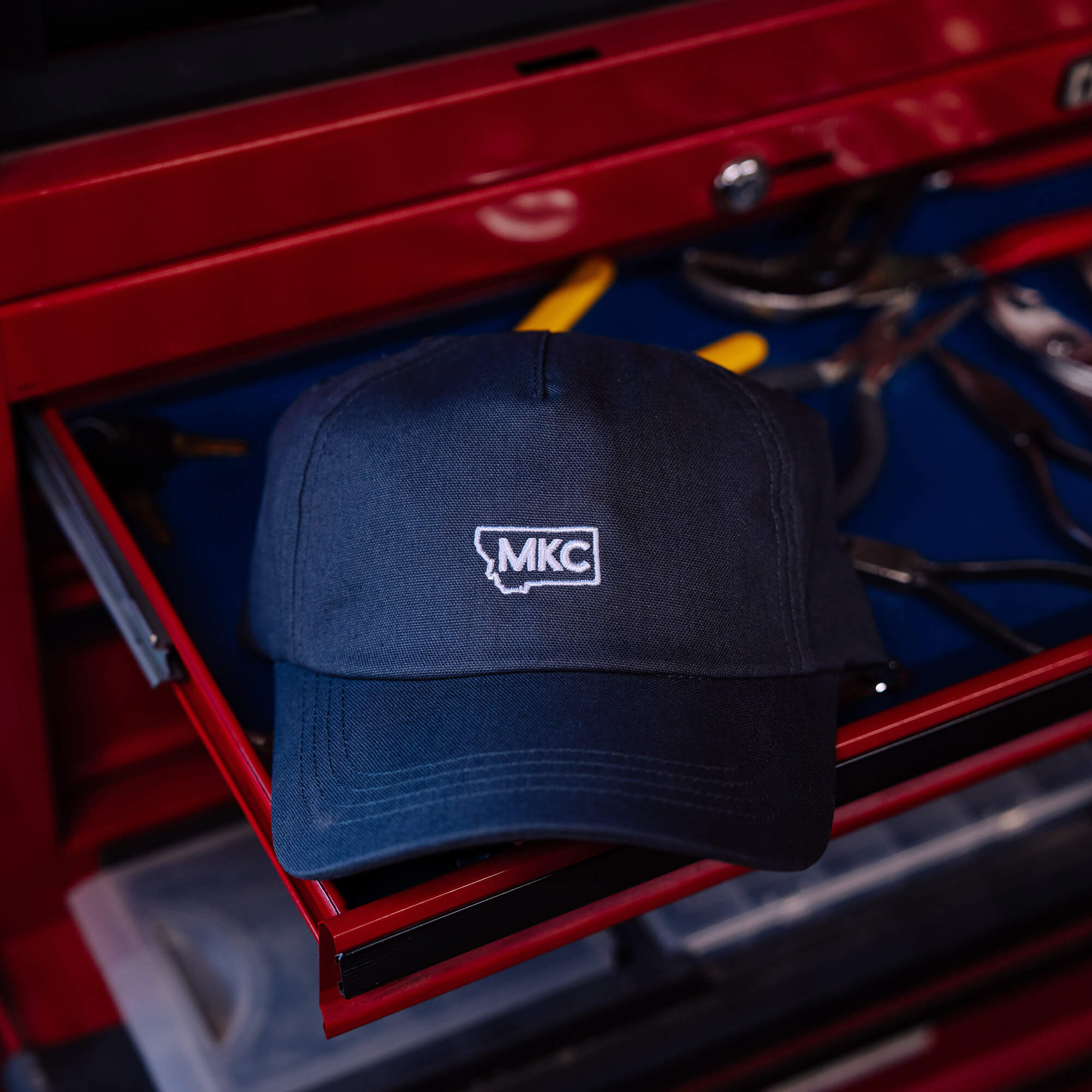 Grey MKC canvas dad hat resting on a toolbox, featuring the MKC logo for outdoor enthusiasts and professionals.