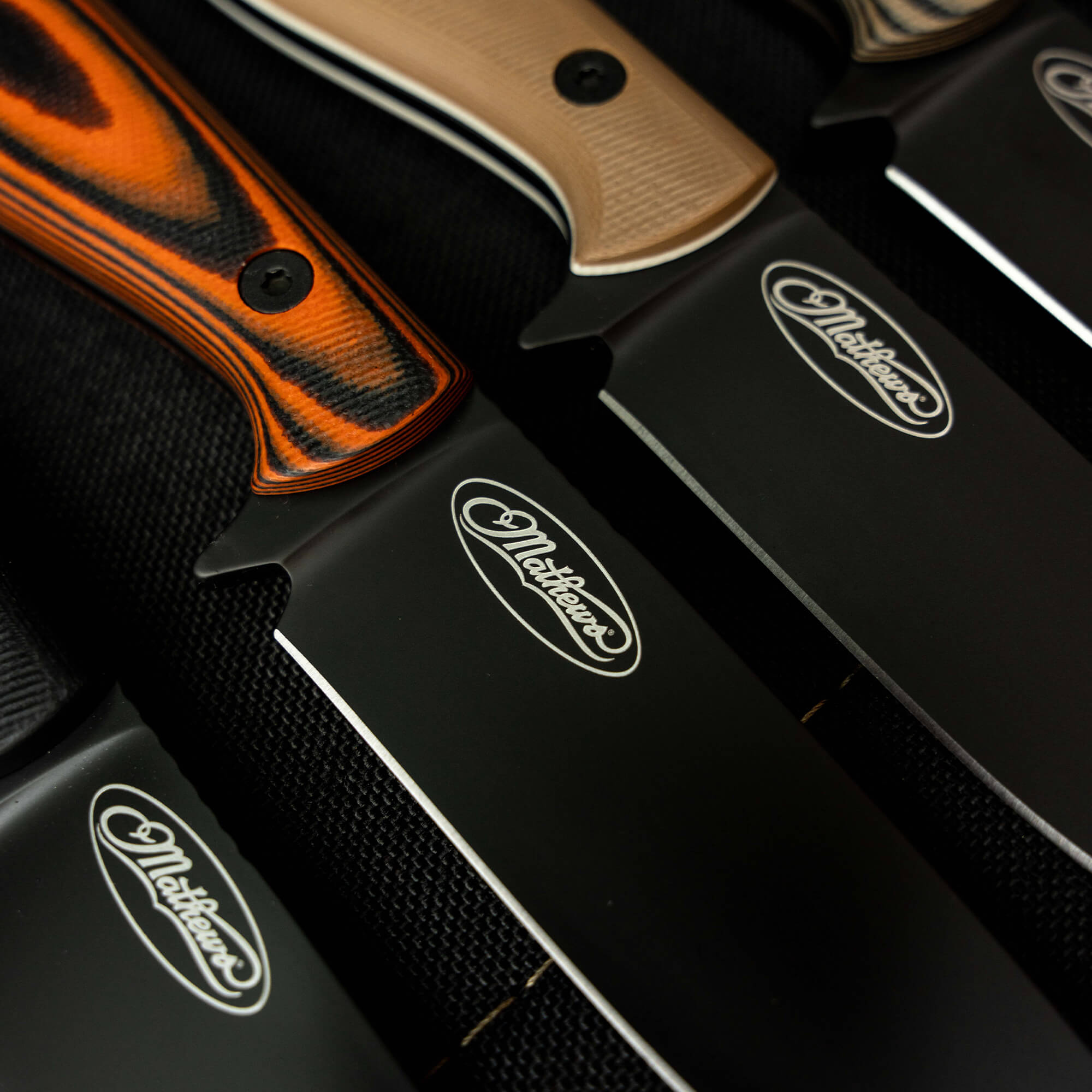 Close-up of Mathews Archery MKC Whitetail knives featuring distinct handles and sleek black blades, showcasing craftsmanship.