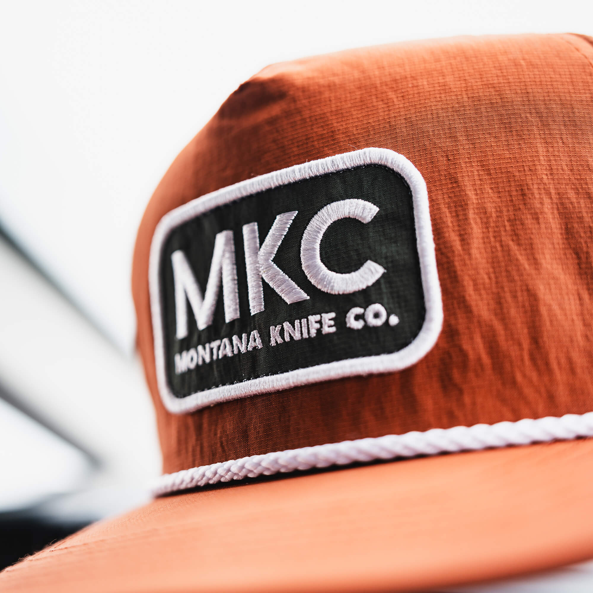 Rust-colored MKC River Rope Hat featuring a prominent logo patch with "Montana Knife Co." for outdoor enthusiasts.