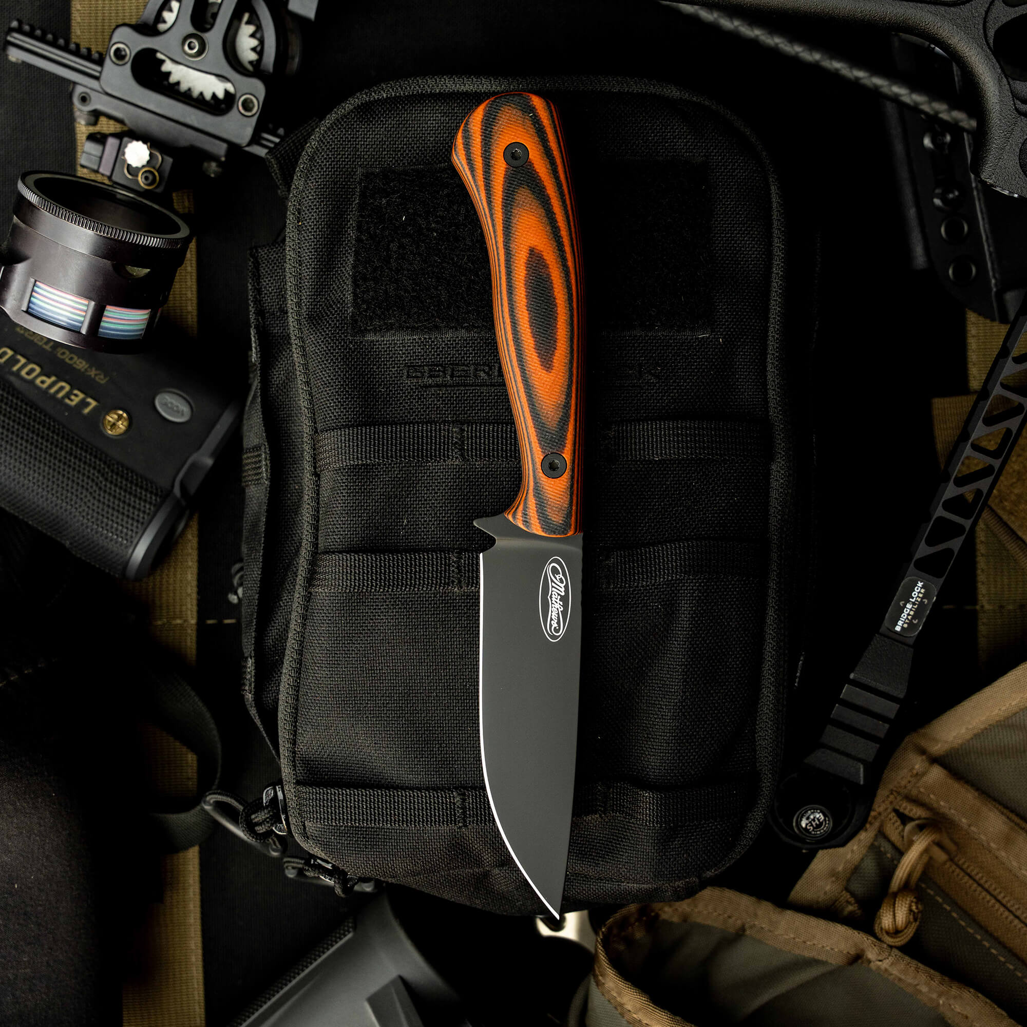 Mathews Archery MKC Whitetail knife with a black blade and orange-brown handle on a tactical pouch. Ideal for hunters.