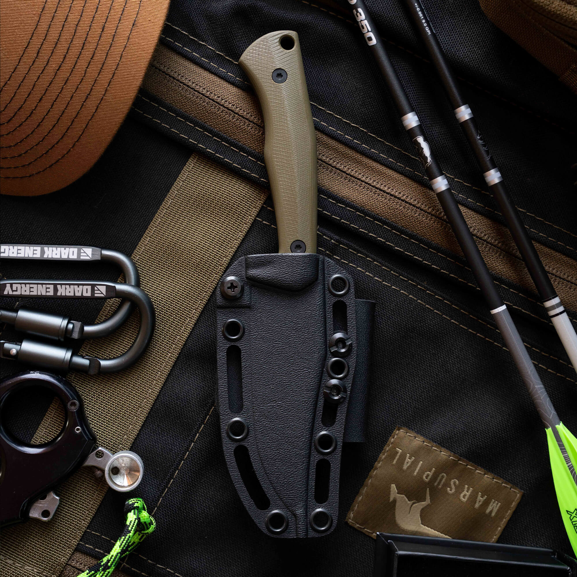 Montana Knife Company's Nock On Triumph Pro knife with a green handle in a black sheath, surrounded by outdoor gear.