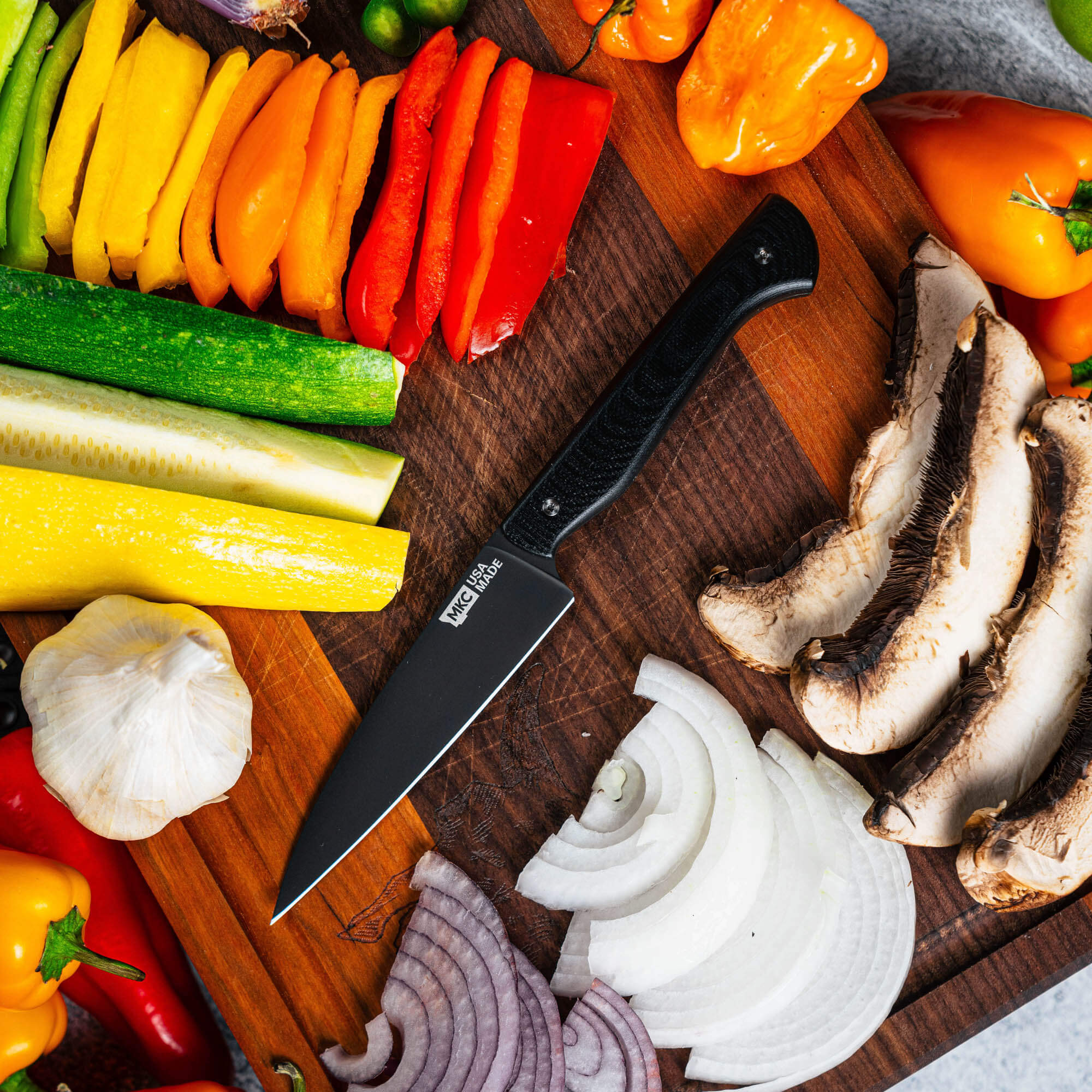 Montana Knife Company's Cutbank paring knife in black on a wooden cutting board with colorful sliced vegetables.
