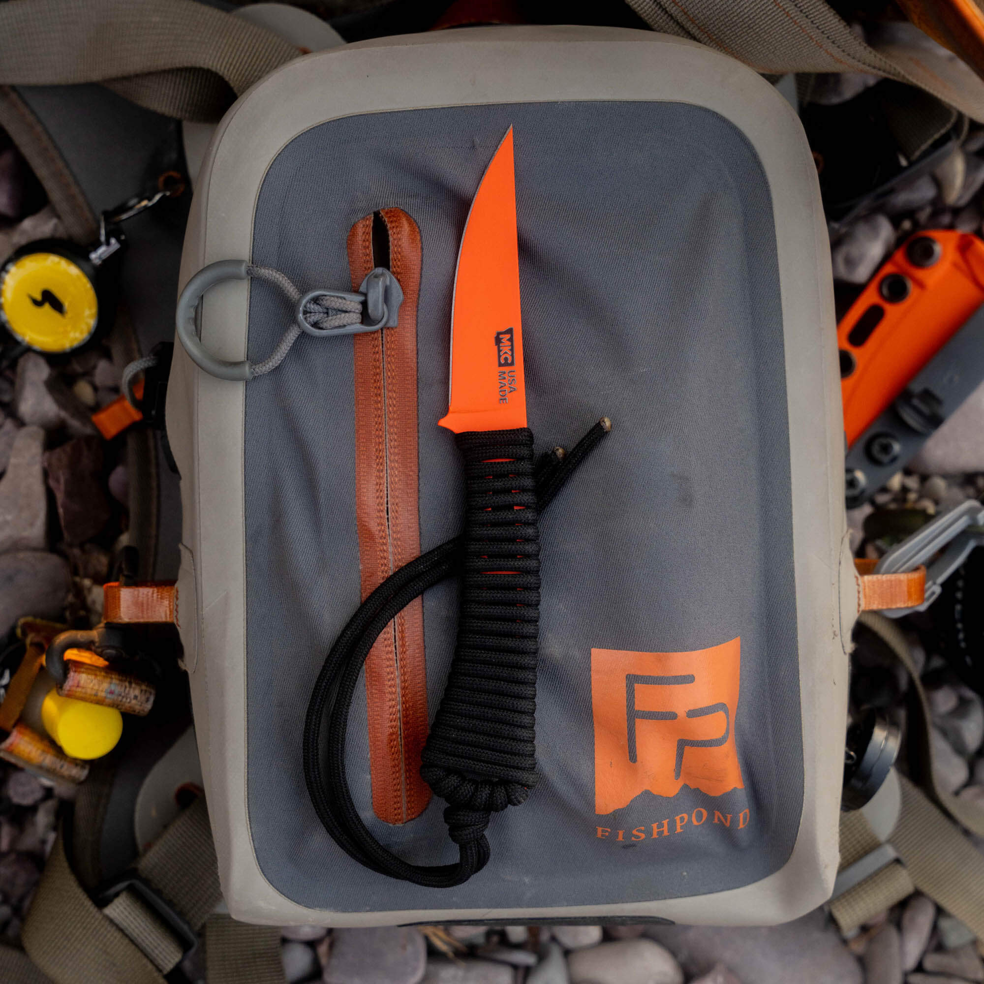 Mini Speedgoat 2.0 knife with Blaze Orange Cerakote finish resting on a Fishpond backpack, showcasing its rugged design.