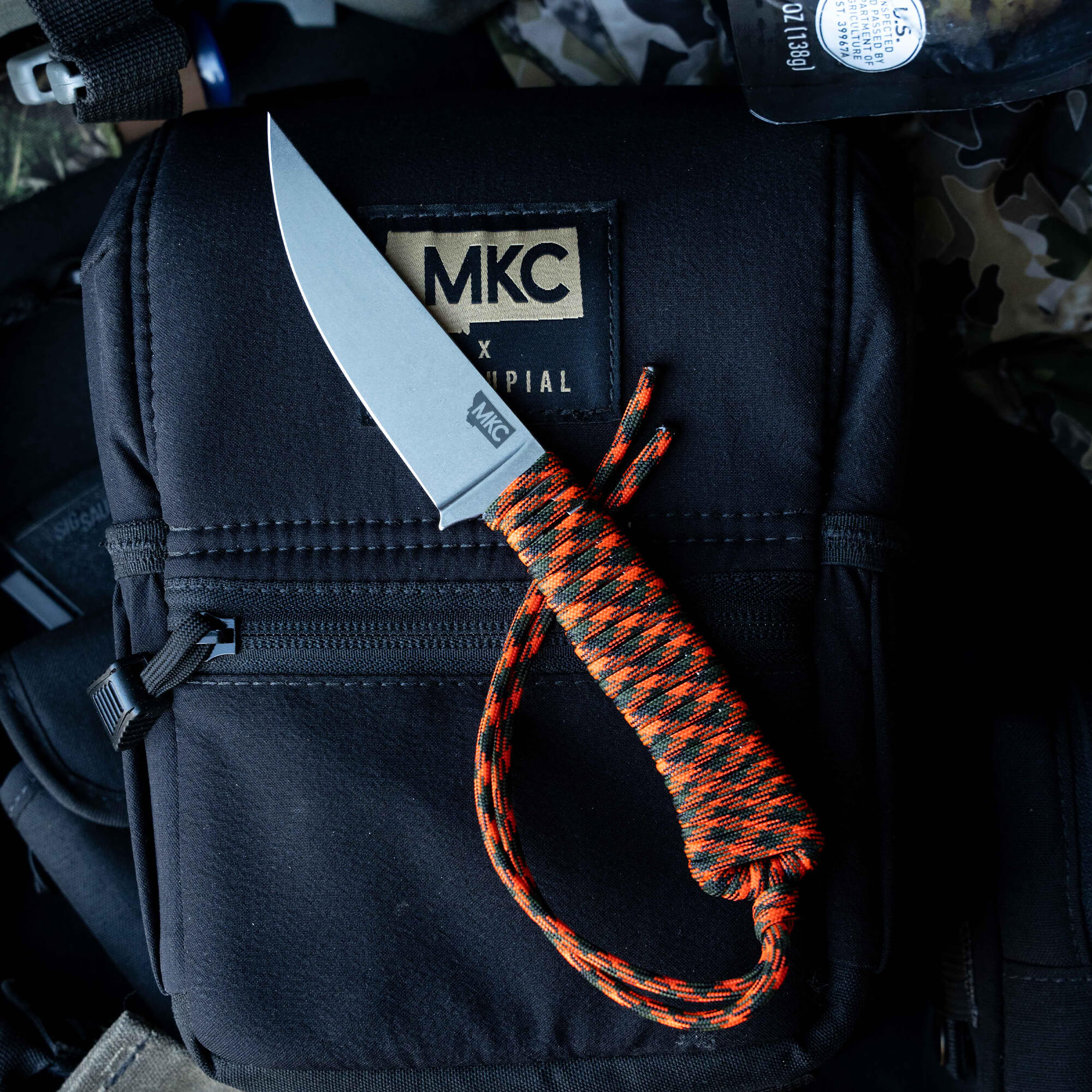 ONX Hunt Magnacut Speedgoat 2.0 knife with an orange and black paracord handle on a tactical bag background.