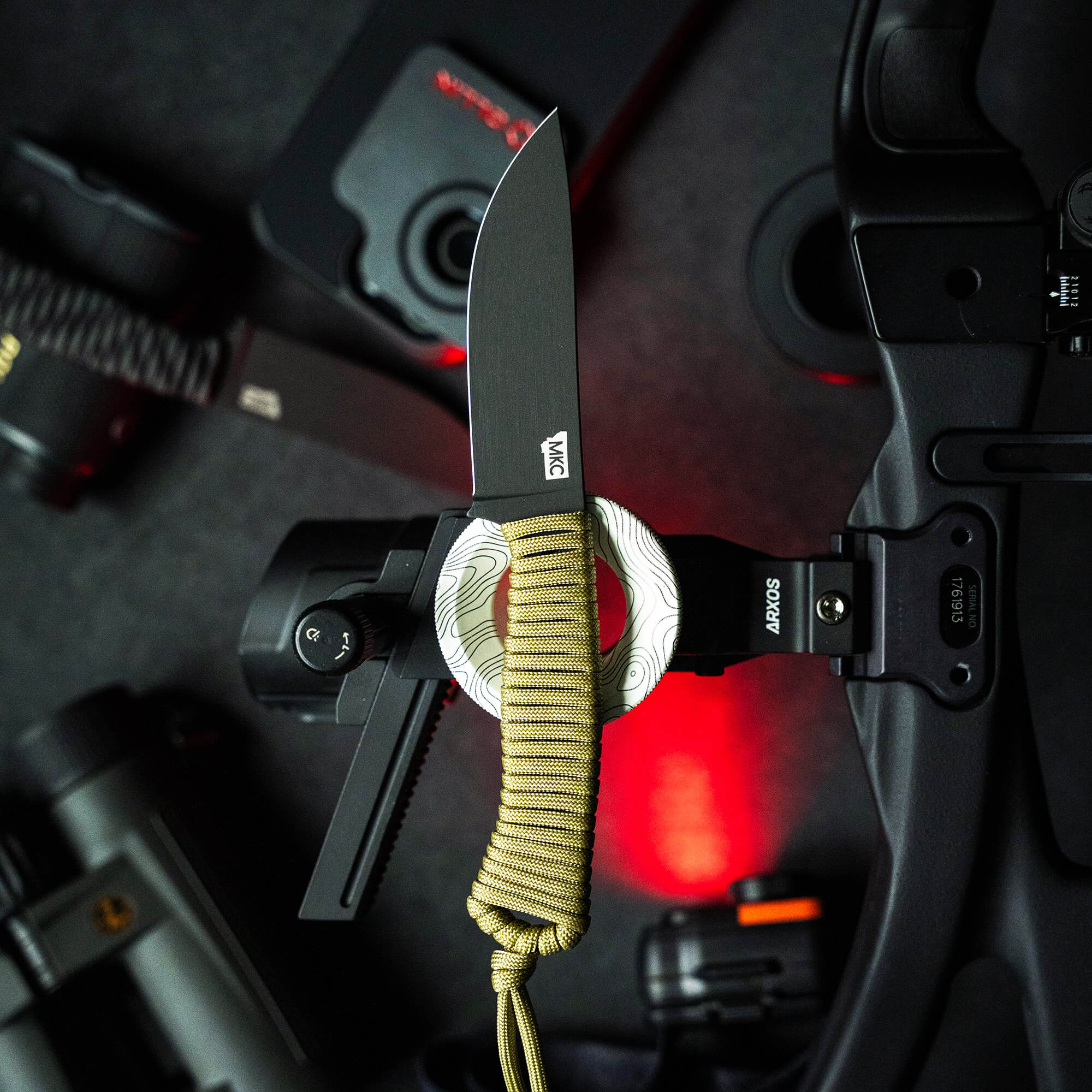 Alt text: "Limited edition Wild Sheep Foundation Stoned Goat 2.0 knife with a dark matte blade and a distinctive handle wrapped in patterned white and grey material with yellow and olive green paracord, displayed on a camera rig with red