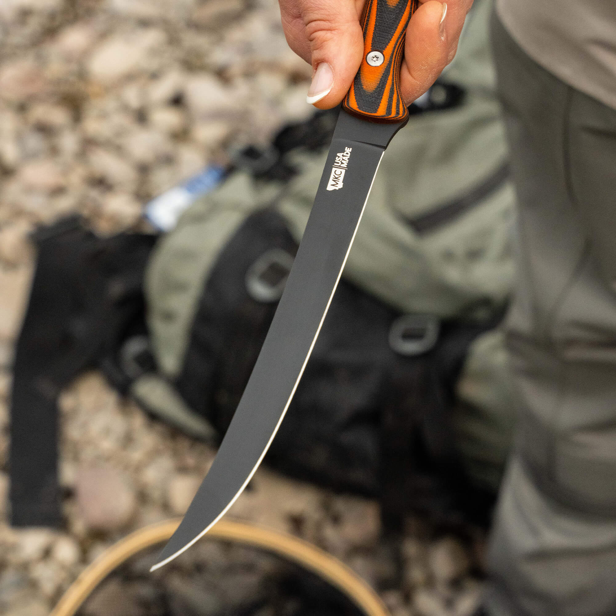 HUK Flathead Fillet knife held by a person, showcasing its long, curved blade and ergonomic handle, with a backpack in the background.