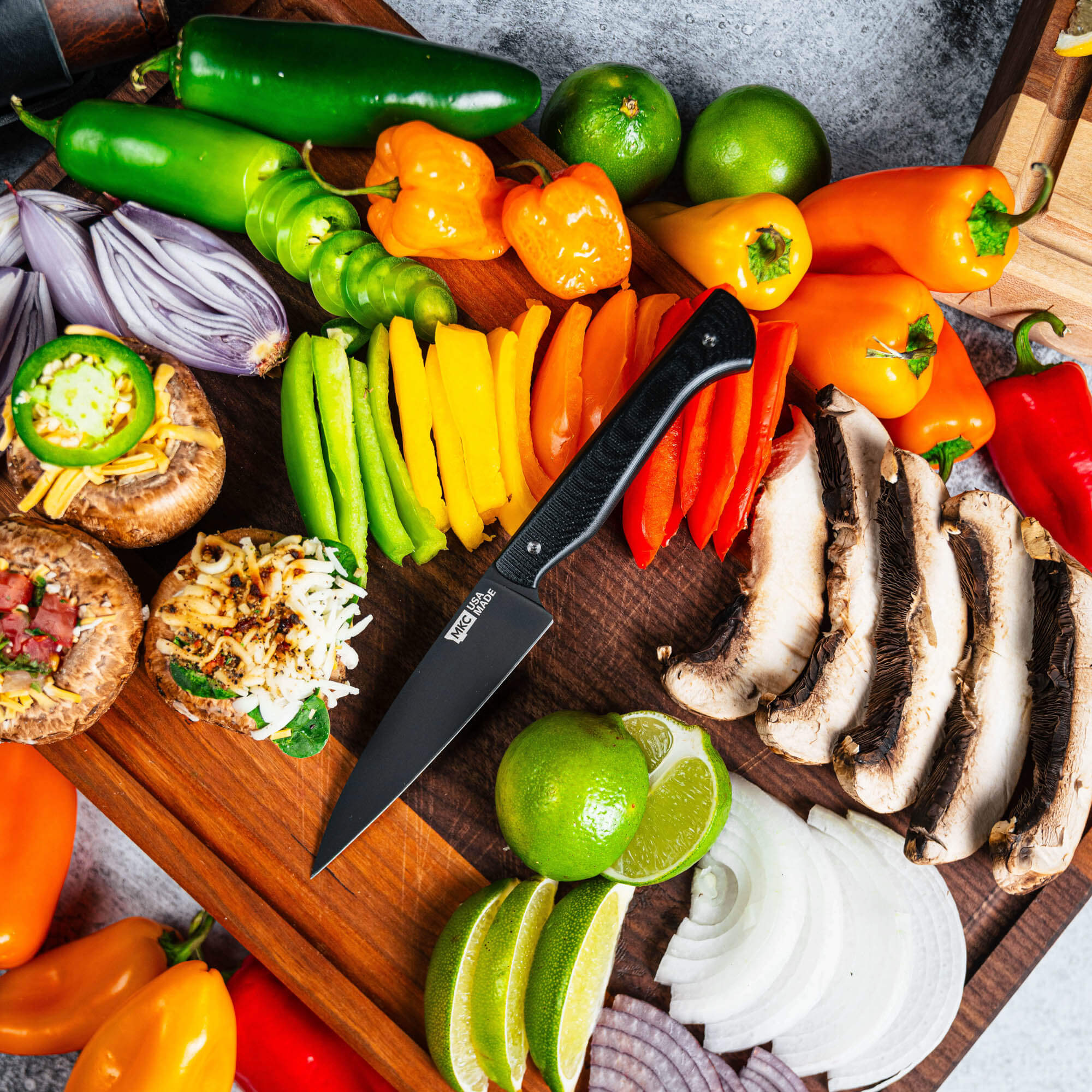 Cutbank paring knife in black positioned among vibrant vegetables and mushrooms on a wooden cutting board.