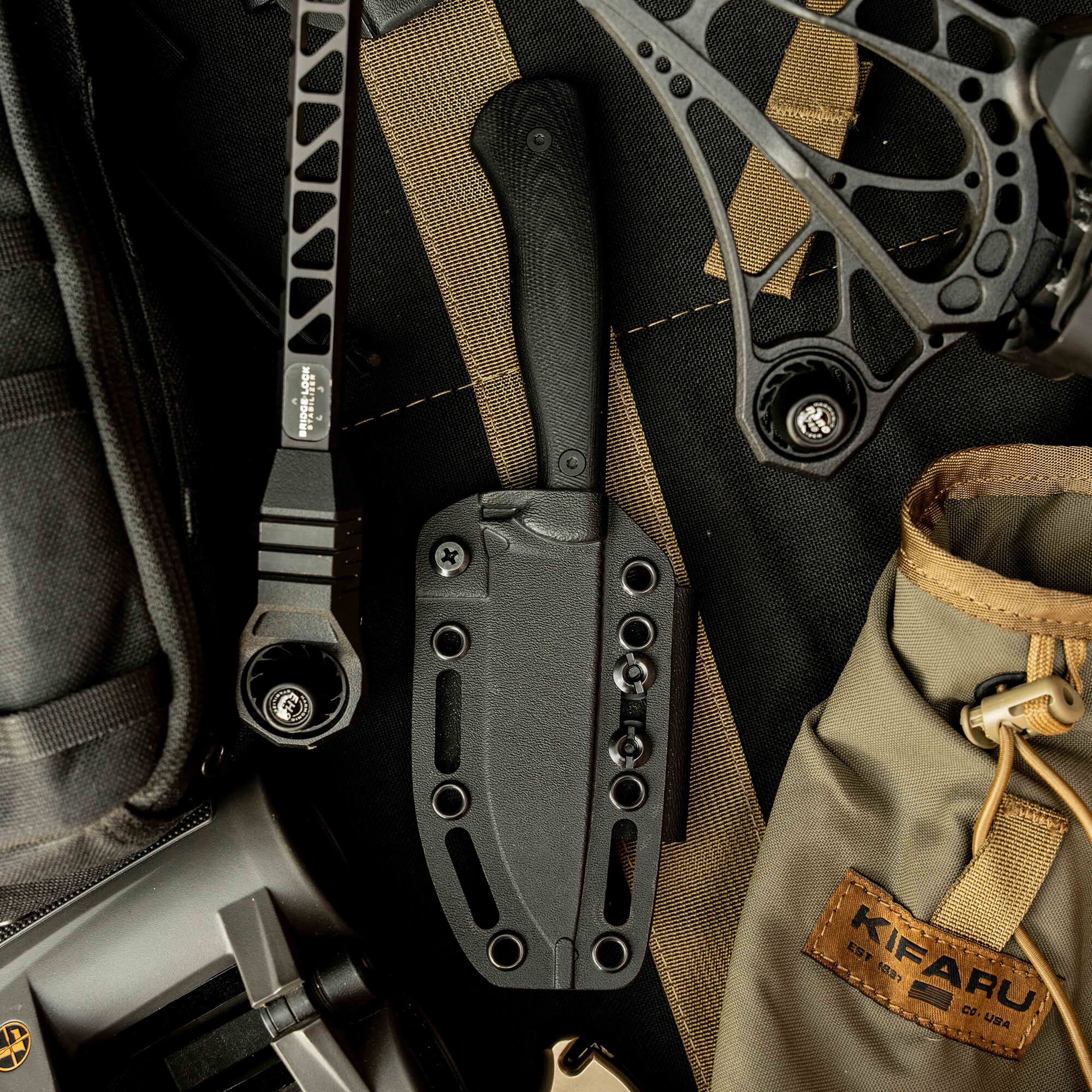 Mathews Archery MKC Whitetail knife with black handle and sheath, surrounded by outdoor gear and accessories.