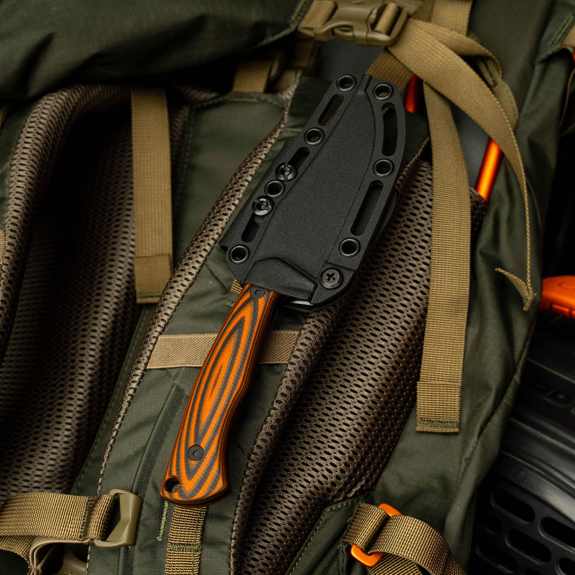 Nock On Triumph Pro knife secured in a tactical backpack, showcasing its black sheath and orange handle.