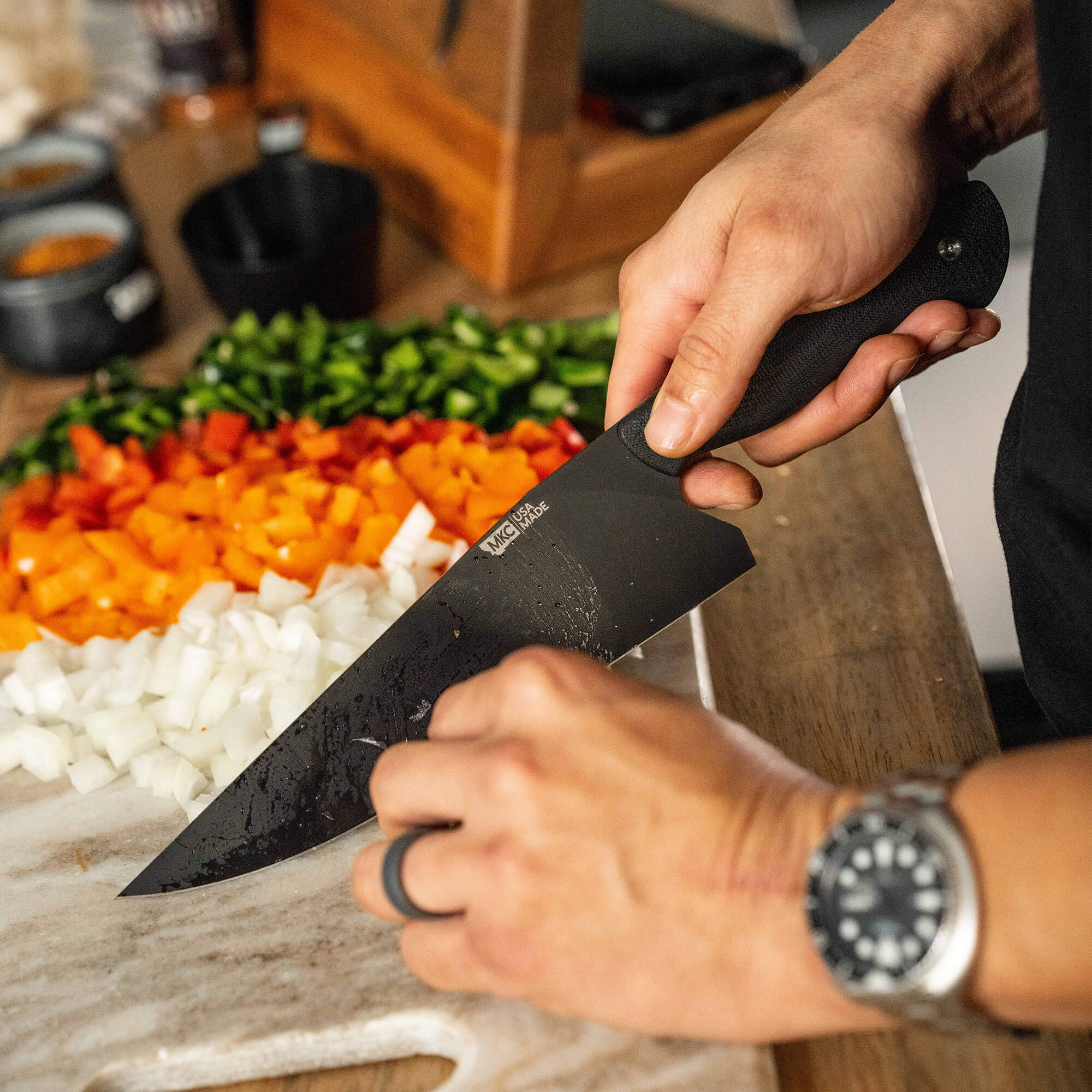 Alt text: "Close-up of a person using the BIGHORN CHEF knife in black, efficiently chopping an assortment of colorful bell peppers and onions on a wooden cutting board."
