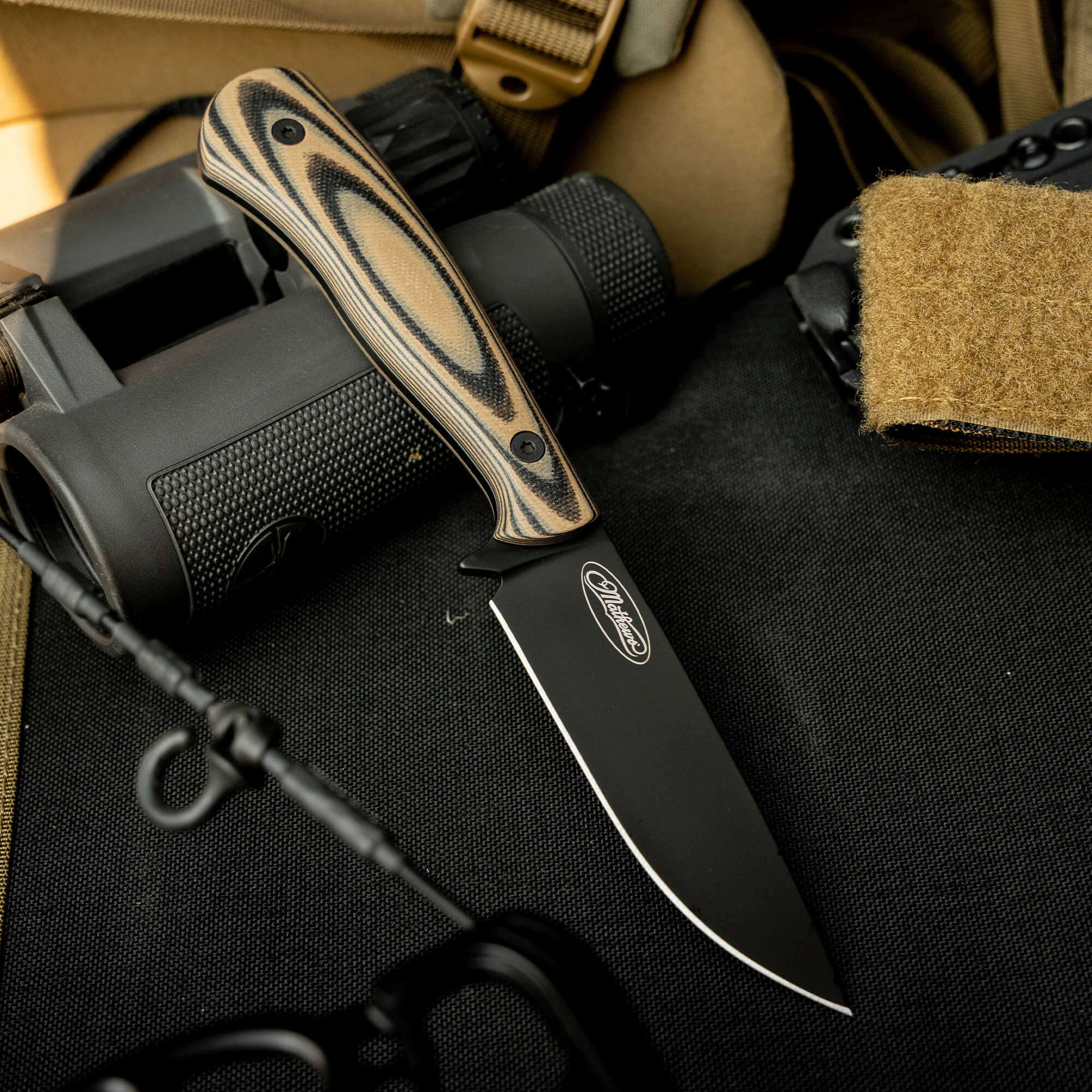 Mathews Archery MKC Whitetail knife with a sleek black blade and patterned handle, resting on tactical gear.