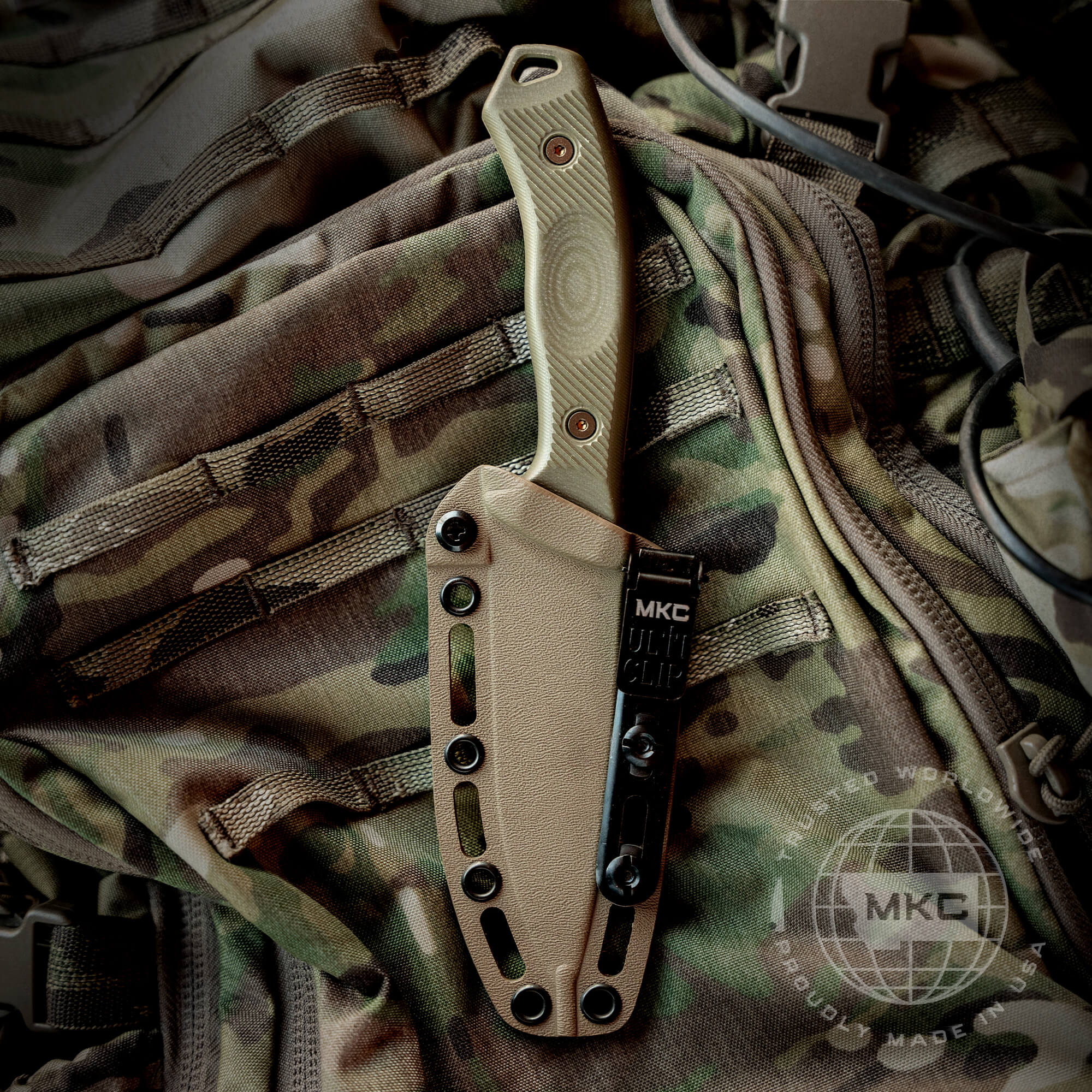 Alt text: "Coyote-colored Additional TF24 Kydex sheath attached to a camouflage backpack, featuring a secure MKC multi-clip and designed for durability and tactical efficiency, with visible rivet reinforcements and multiple attachment points."