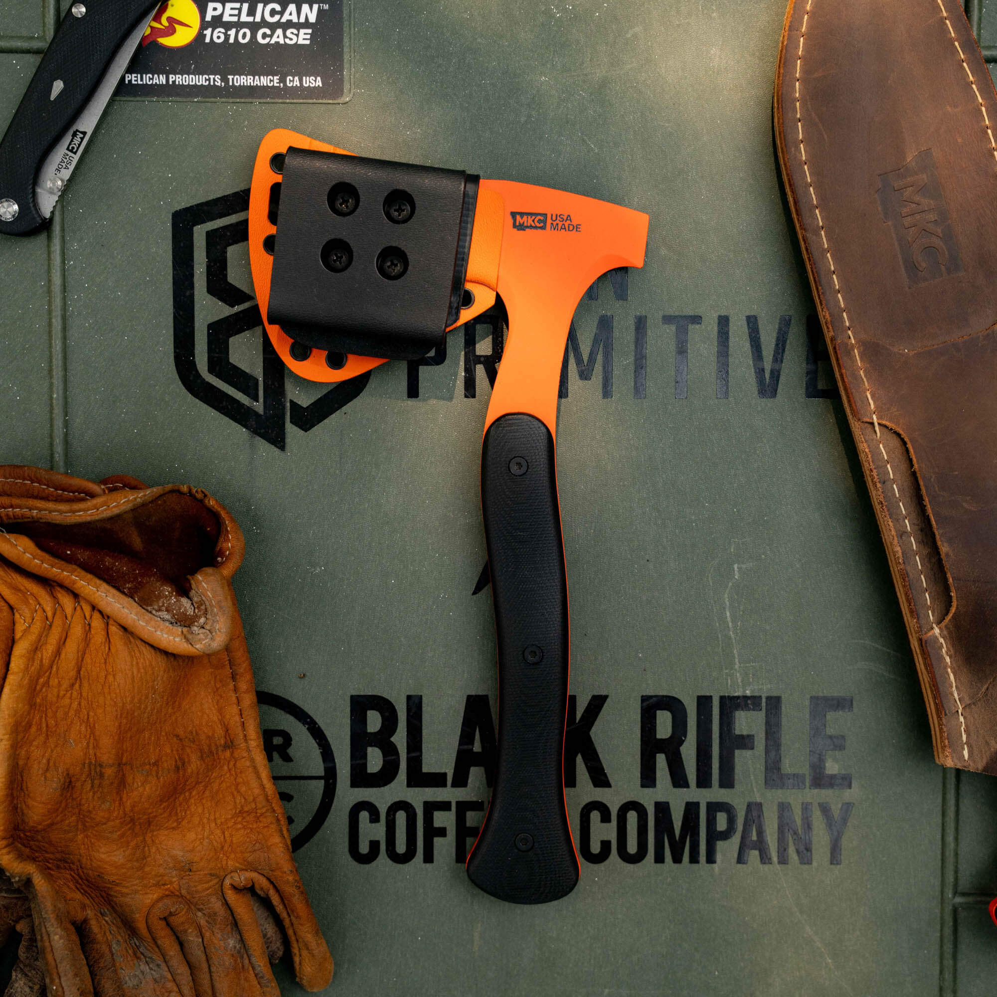 HELLGATE HATCHET with additional Kydex sheath on a textured surface, surrounded by gloves and tools, showcasing its rugged design.