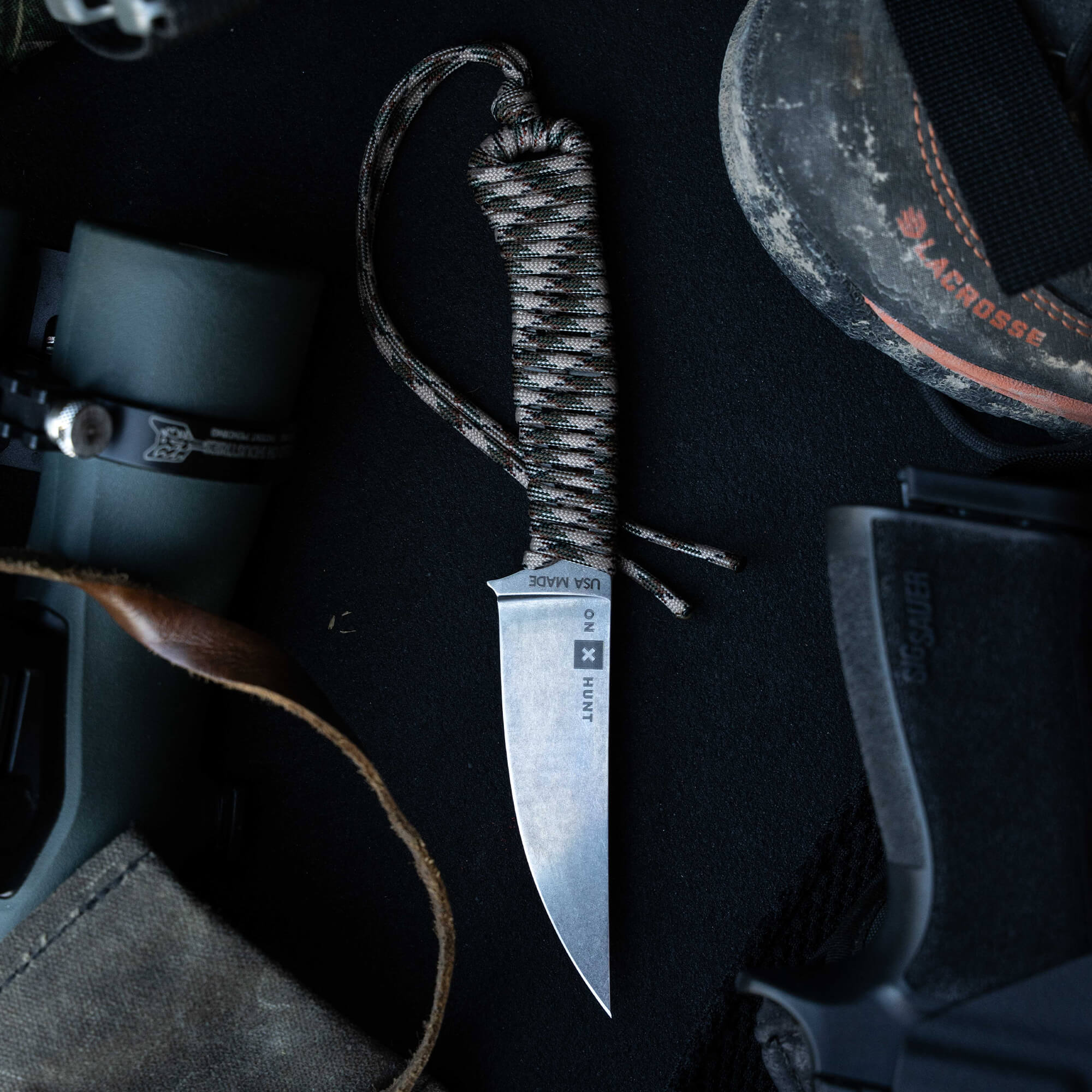 ONX Hunt Magnacut Speedgoat 2.0 knife with a paracord handle, surrounded by outdoor gear, ideal for hunters and outdoor enthusiasts.