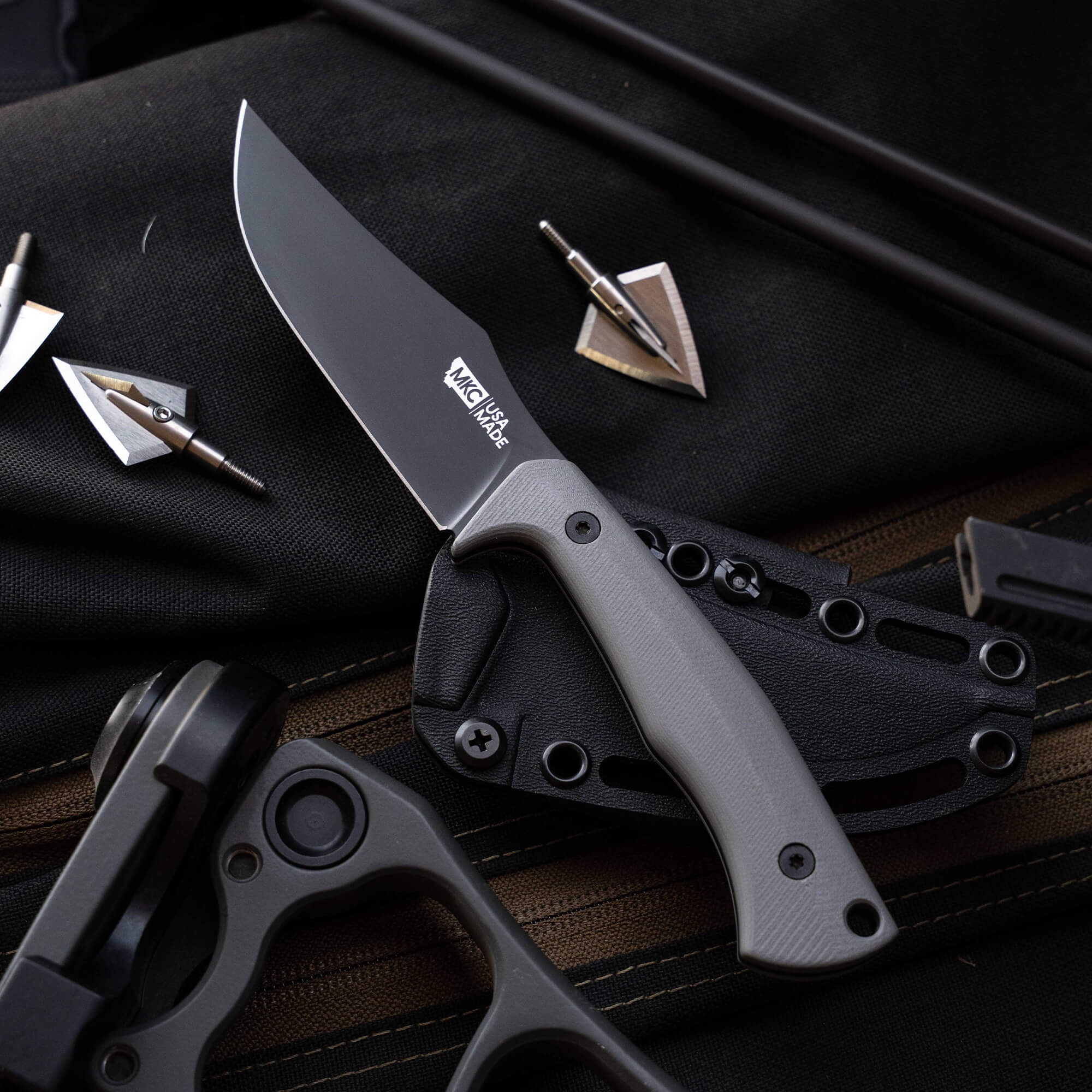 Montana Knife Company's Nock On Triumph Pro knife with a sleek blade and ergonomic handle, set against tactical gear.