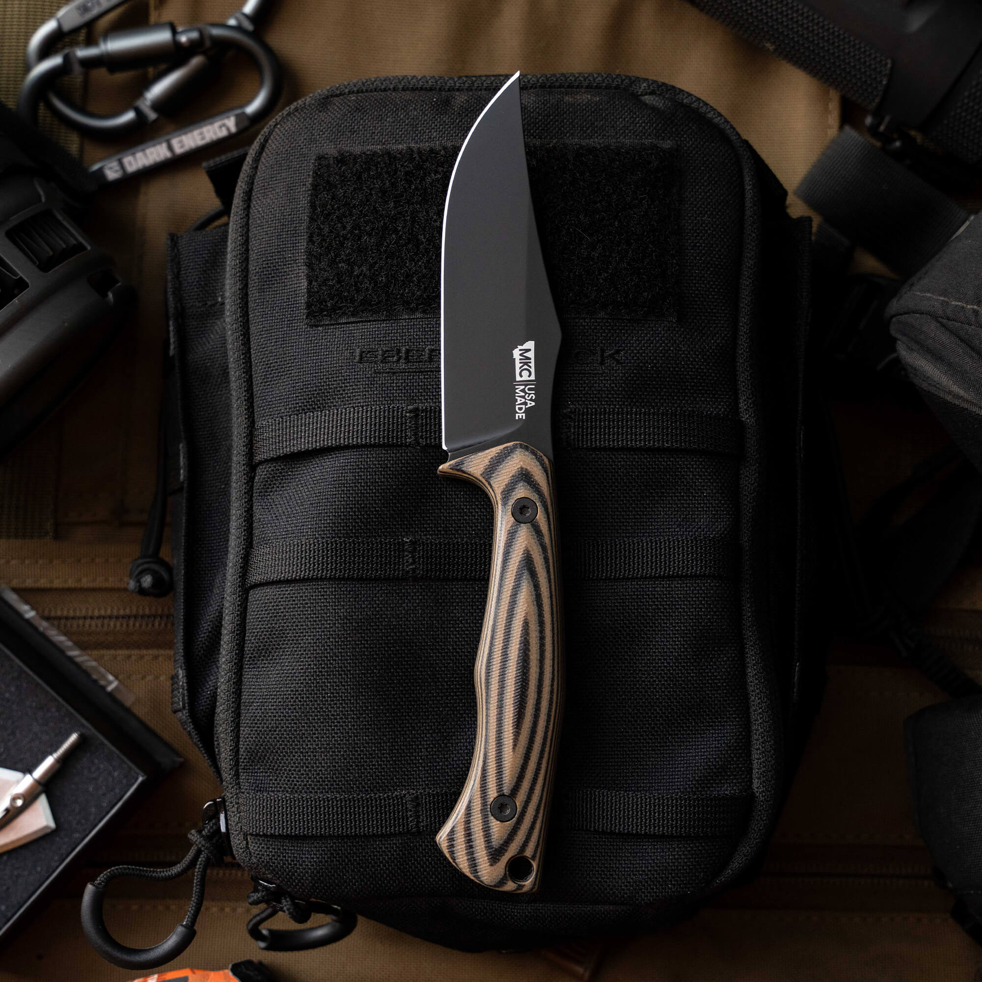 NOCK ON Triumph Pro knife with a black blade and striped handle, displayed on a tactical black bag and gear.