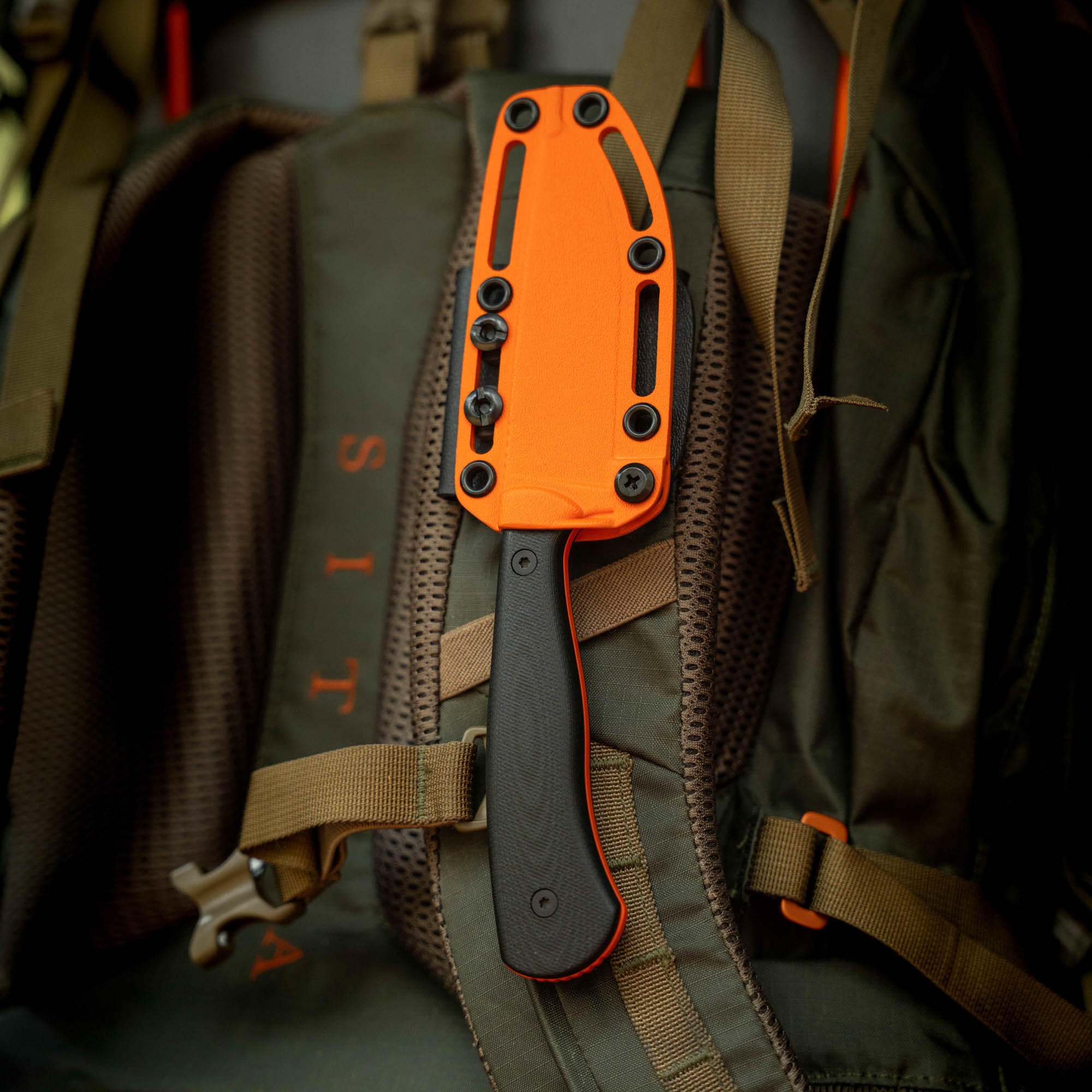 Additional Kydex sheath for the Whitetail knife, featuring an orange exterior and black handle, attached to a backpack.