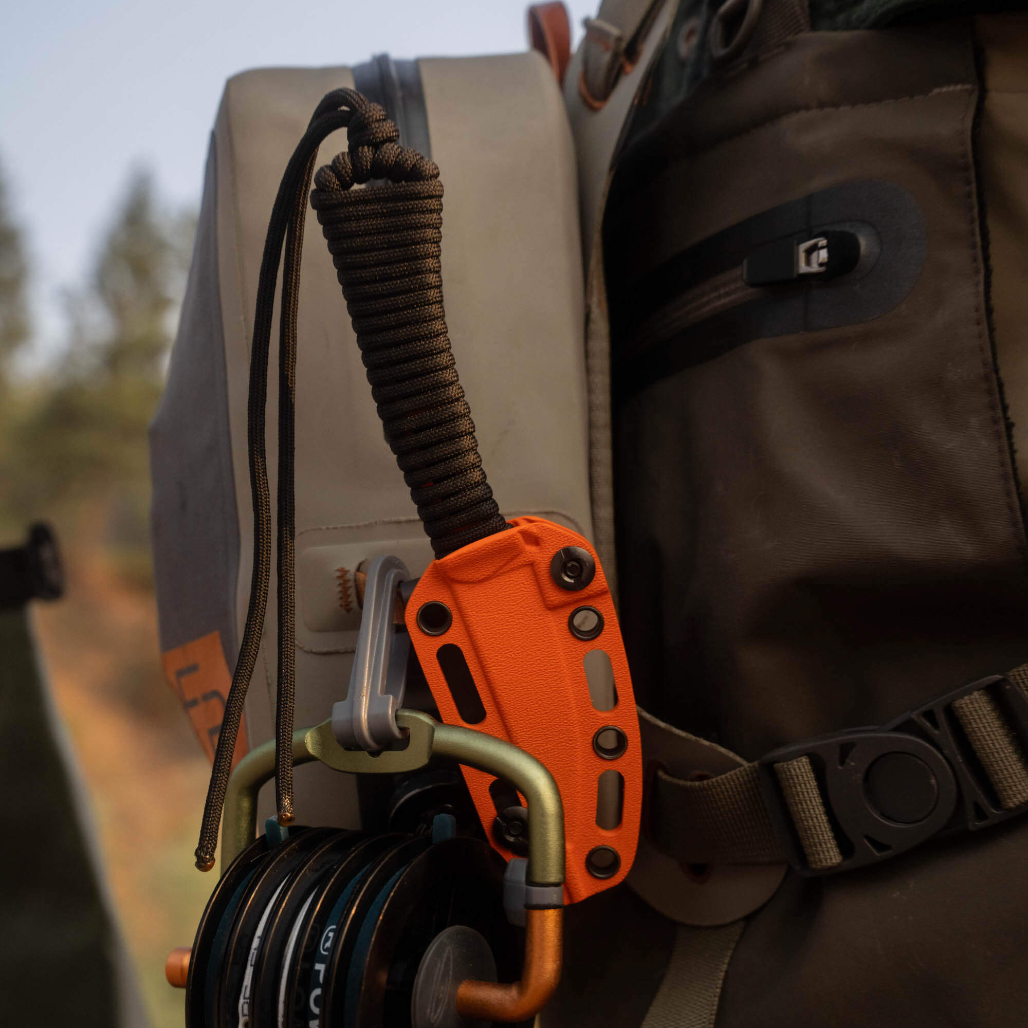 Blaze orange Cerakote MINI SPEEDGOAT 2.0 knife attached to a backpack with gear, showcasing its rugged design.