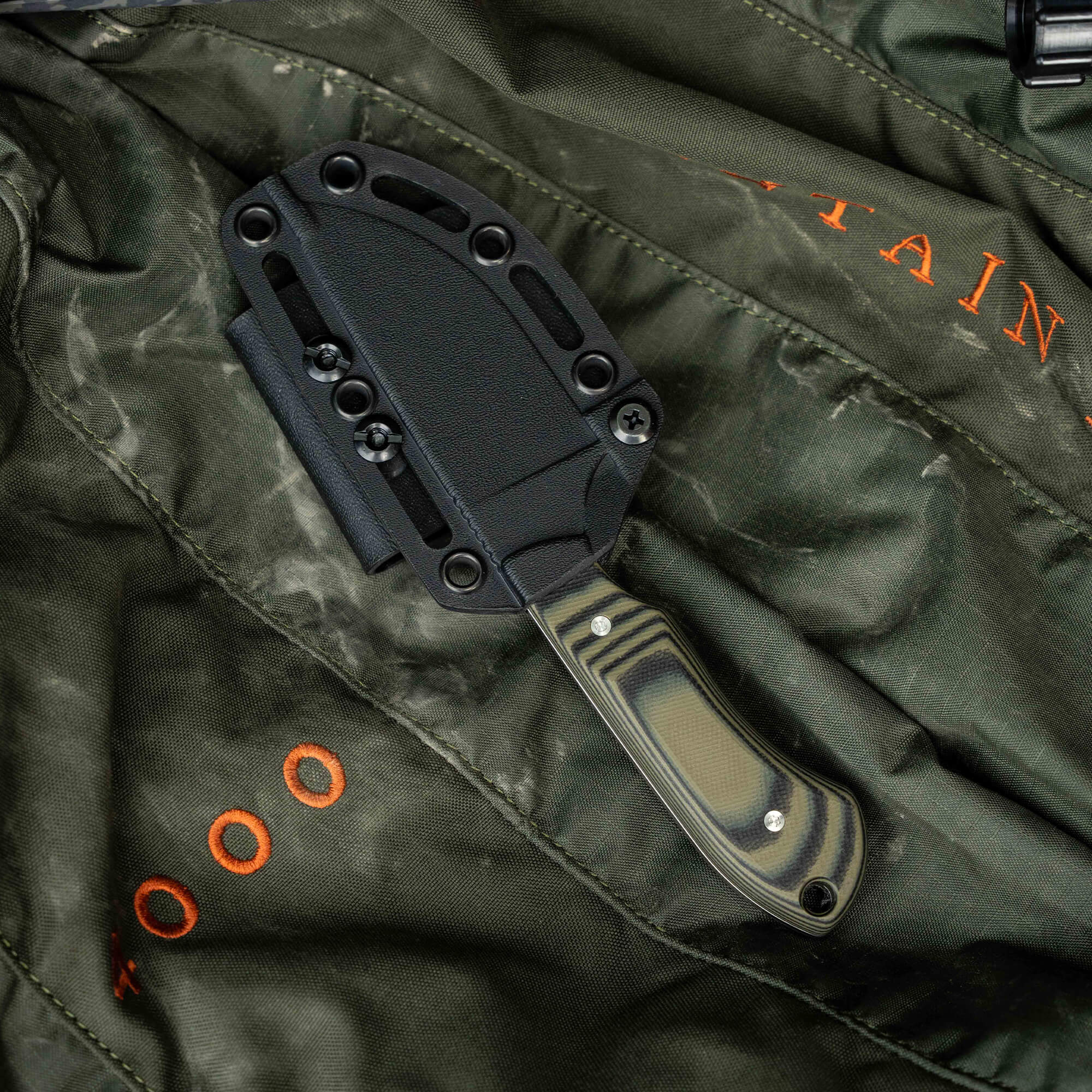 Montana Knife Company's sold-out Live Wild Elk Knife with a camo handle and sheath on a rugged green background.