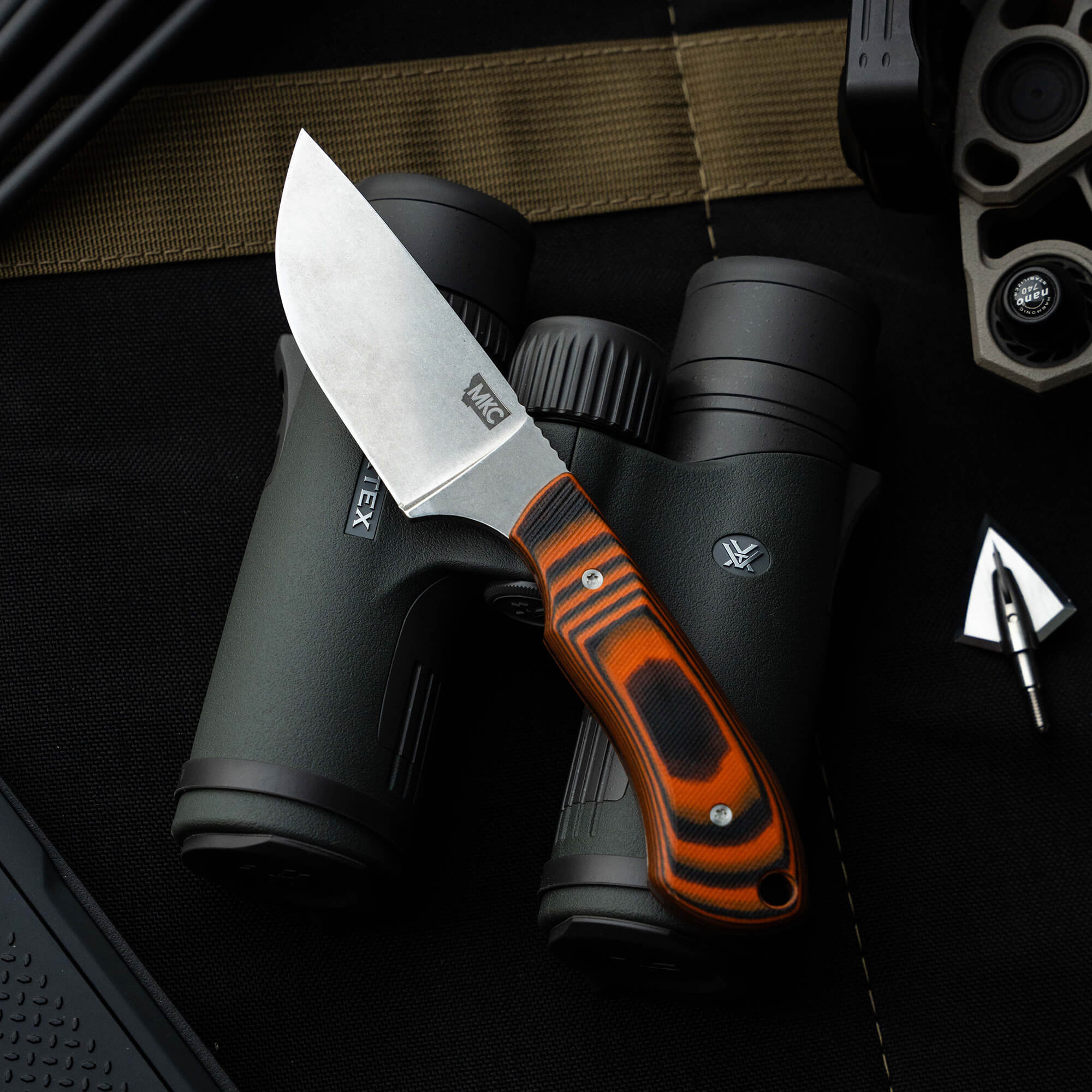 Montana Knife Company's Live Wild Elk Knife featuring a sleek blade and vibrant handle, resting beside binoculars.