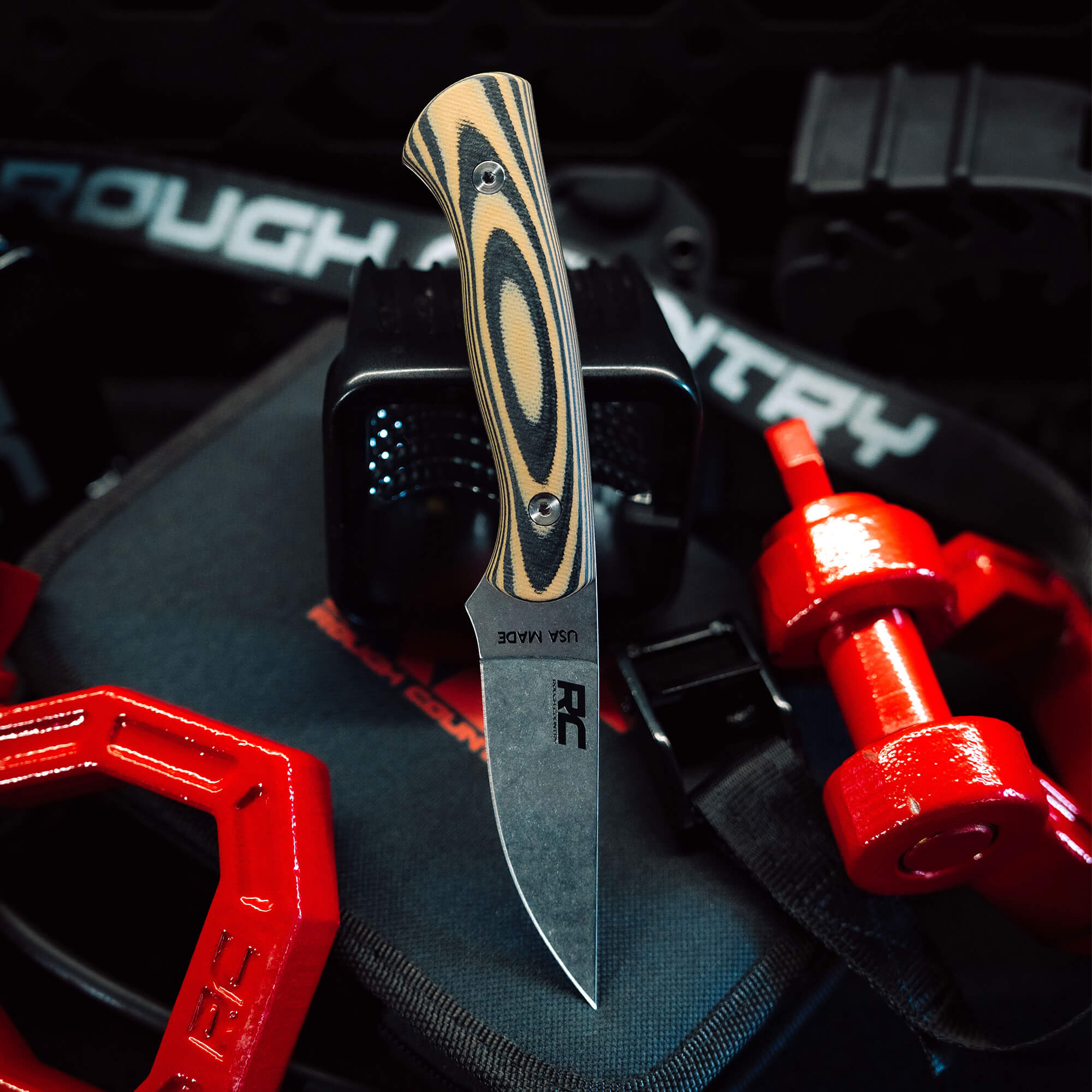 Rough Country Magnacut Blackfoot 2.0 knife with a striking handle design, displayed on a gym mat with weights.