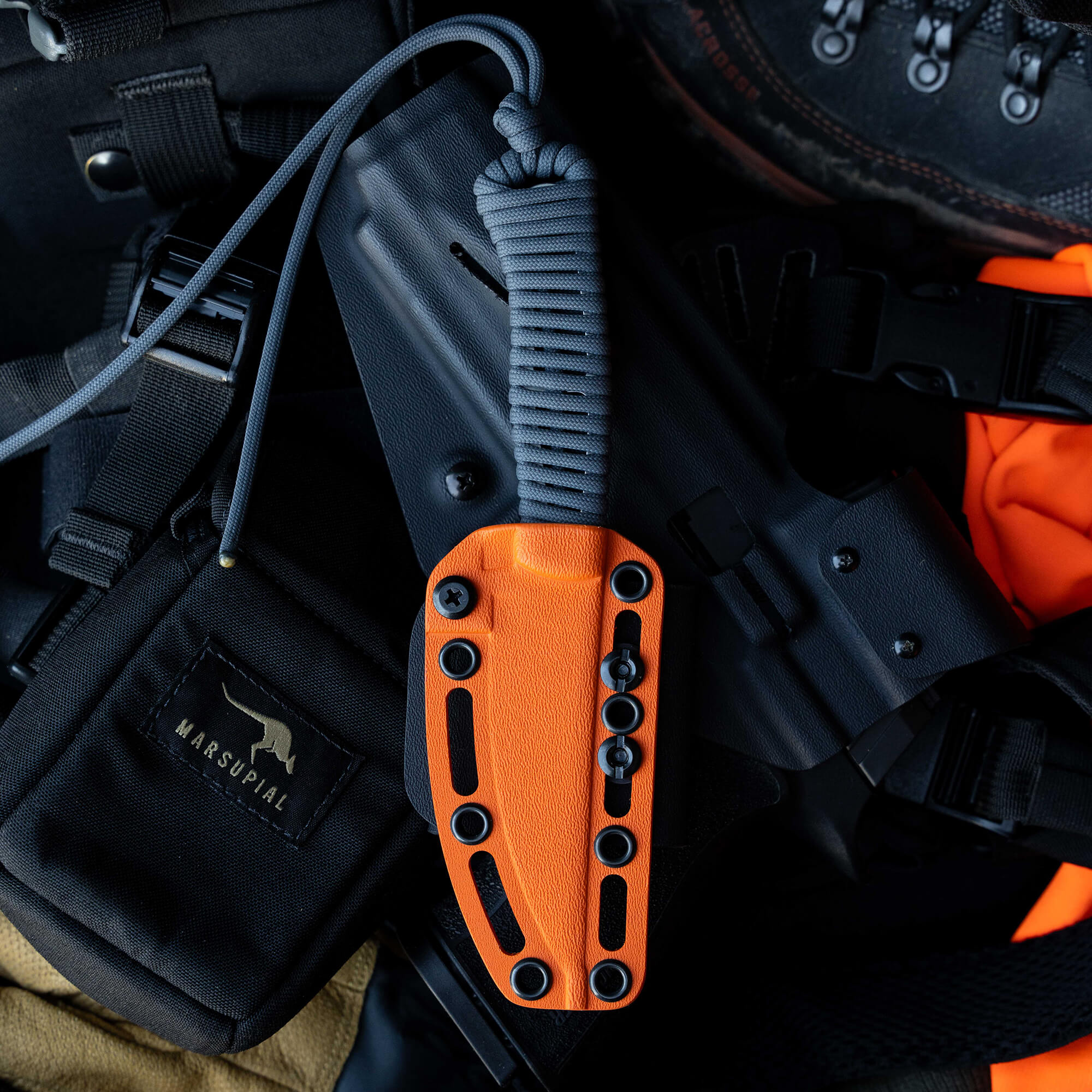 ONX Hunt Magnacut Speedgoat 2.0 knife with an orange handle and gray paracord, set against tactical gear and clothing.