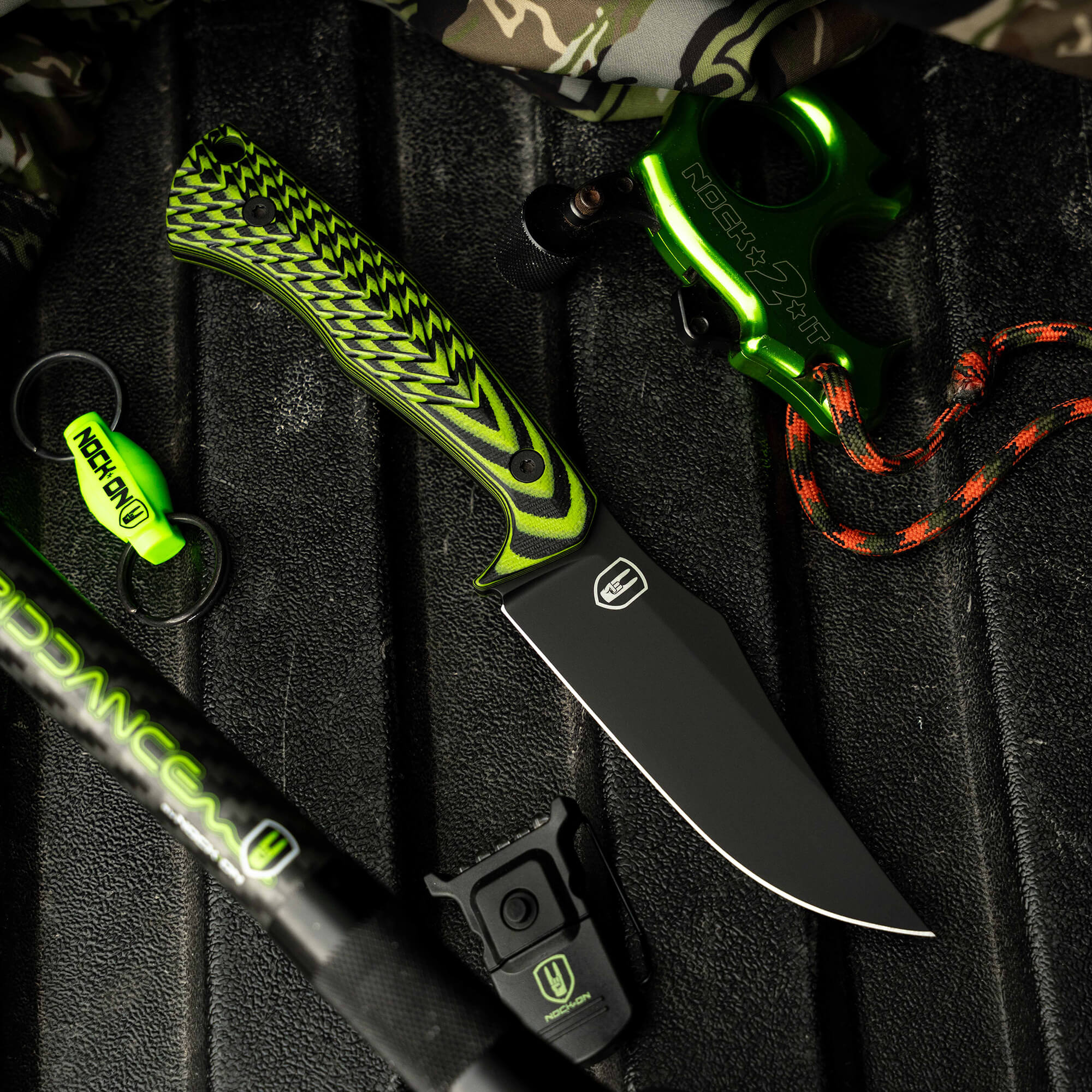 Nock On Triumph Pro knife with a vibrant green and black handle, surrounded by outdoor gear and accessories.
