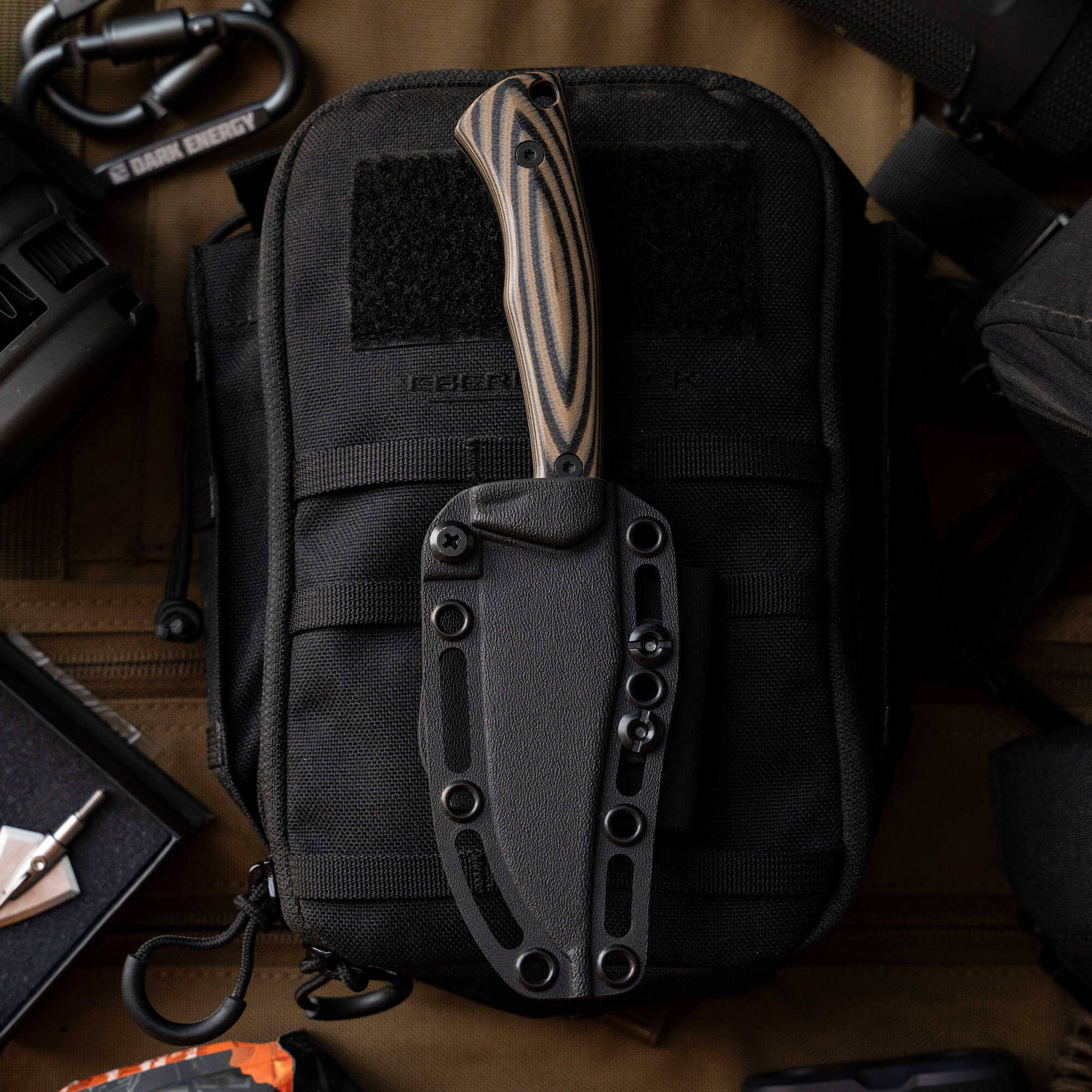 Nock On Triumph Pro knife with a black sheath, resting on a tactical bag, showcasing its sleek design and handle.