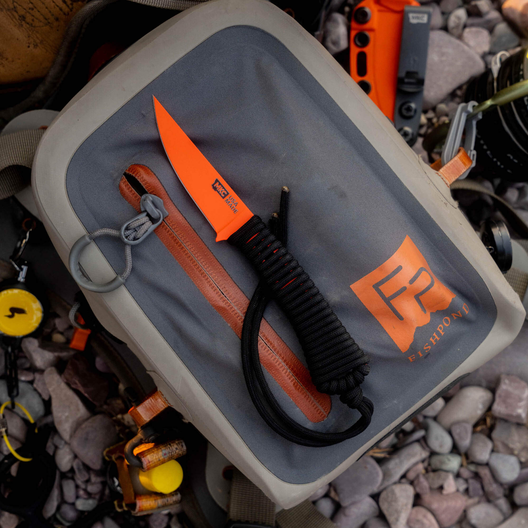 Blaze orange Cerakote MINI SPEEDGOAT 2.0 knife on a gray Fishpond bag, showcasing its durable design for outdoor use.