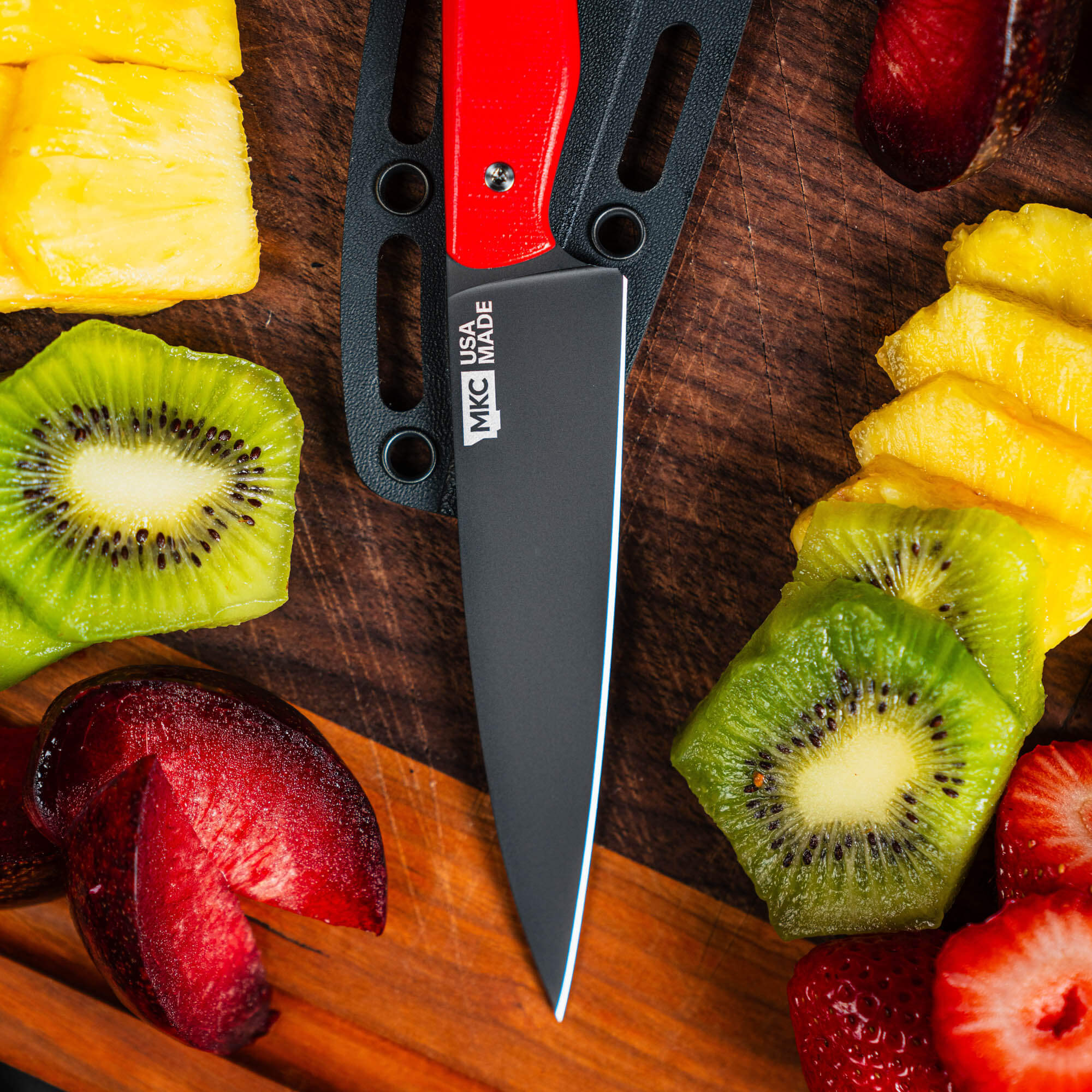 Montana Knife Company's Cutbank paring knife with a red handle, surrounded by fresh sliced fruits on a wooden cutting board.