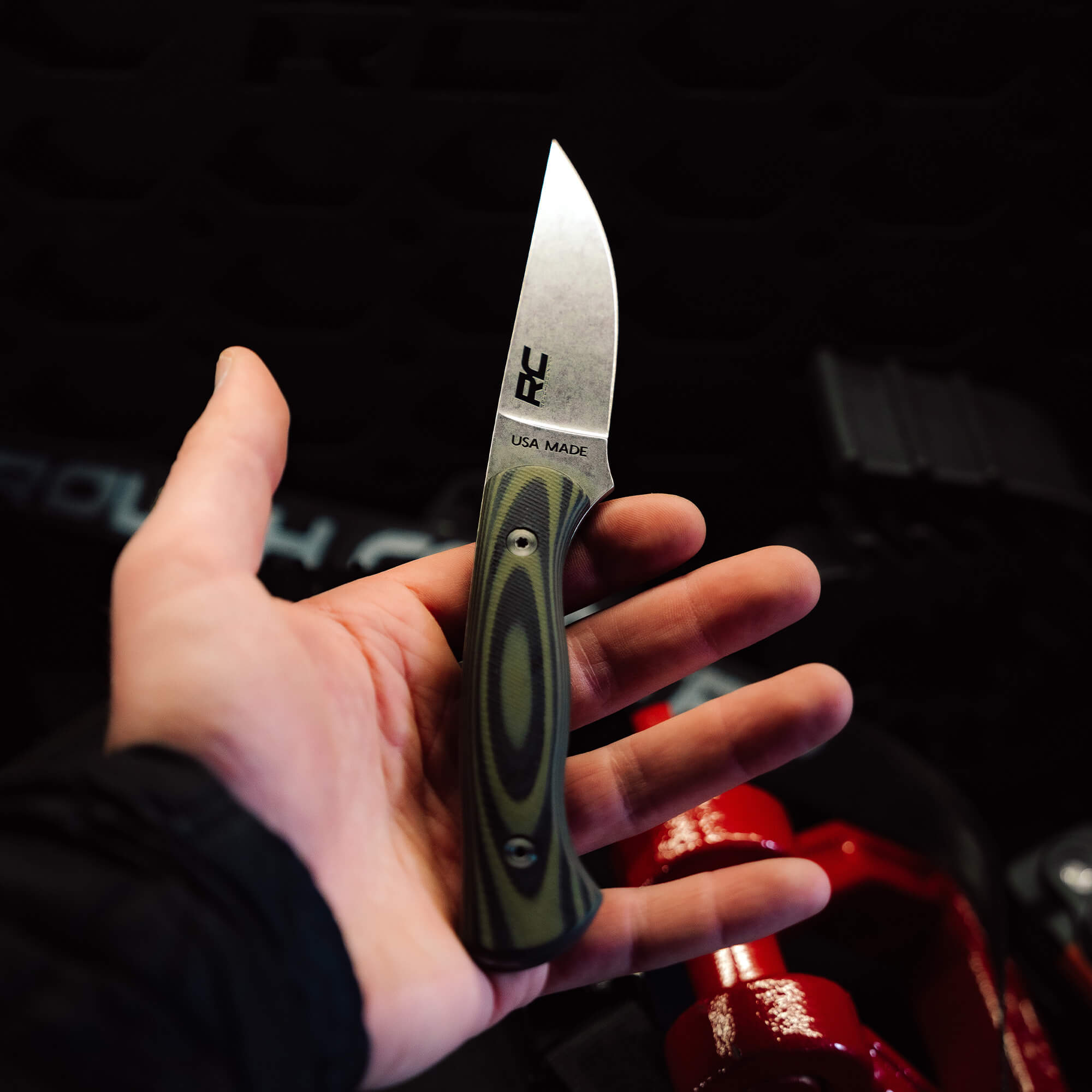 Hand holding the Rough Country Magnacut Blackfoot 2.0 knife, featuring a sleek blade and textured green handle, USA made.