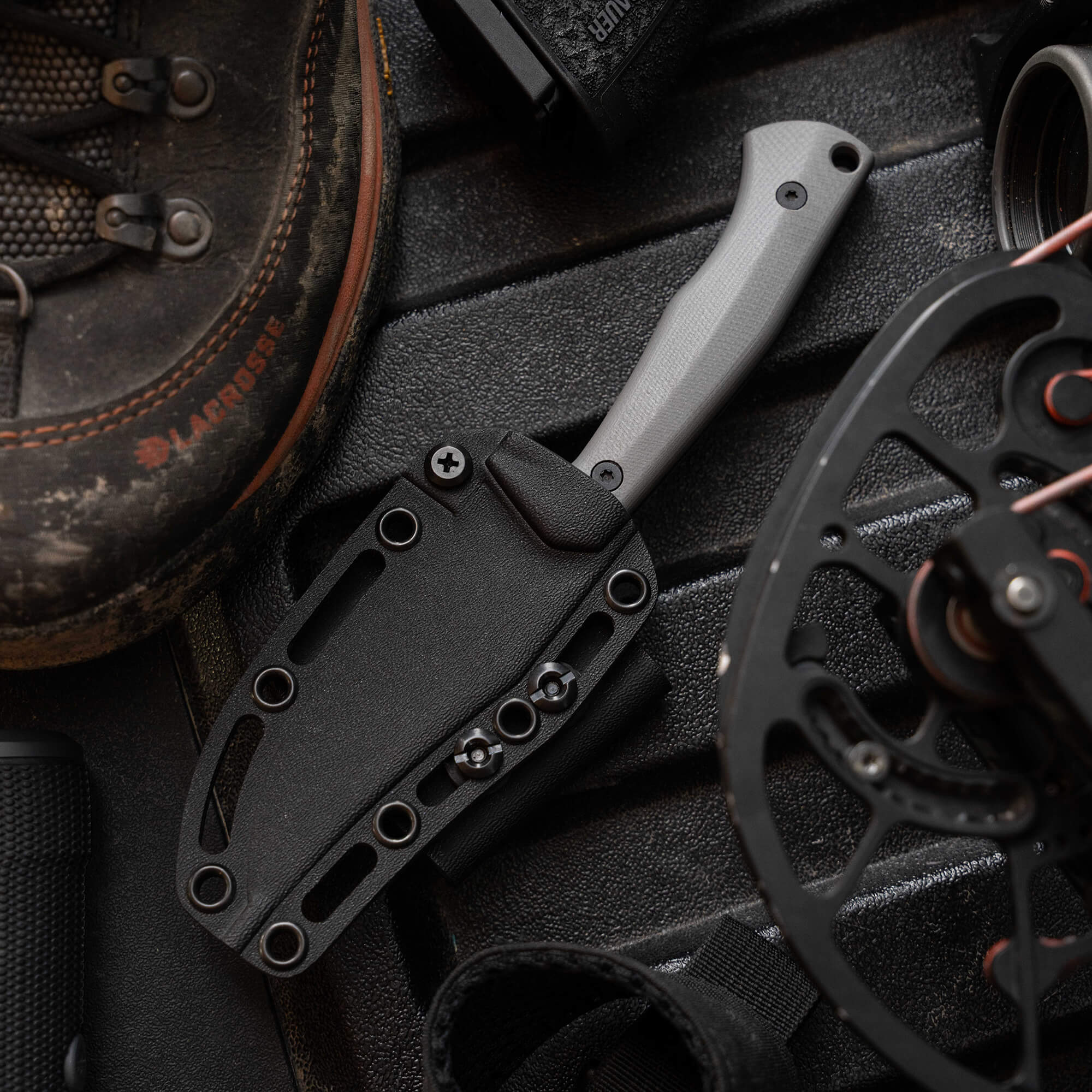 Montana Knife Company's Nock On Triumph Pro knife in a sheath, surrounded by outdoor gear and equipment.
