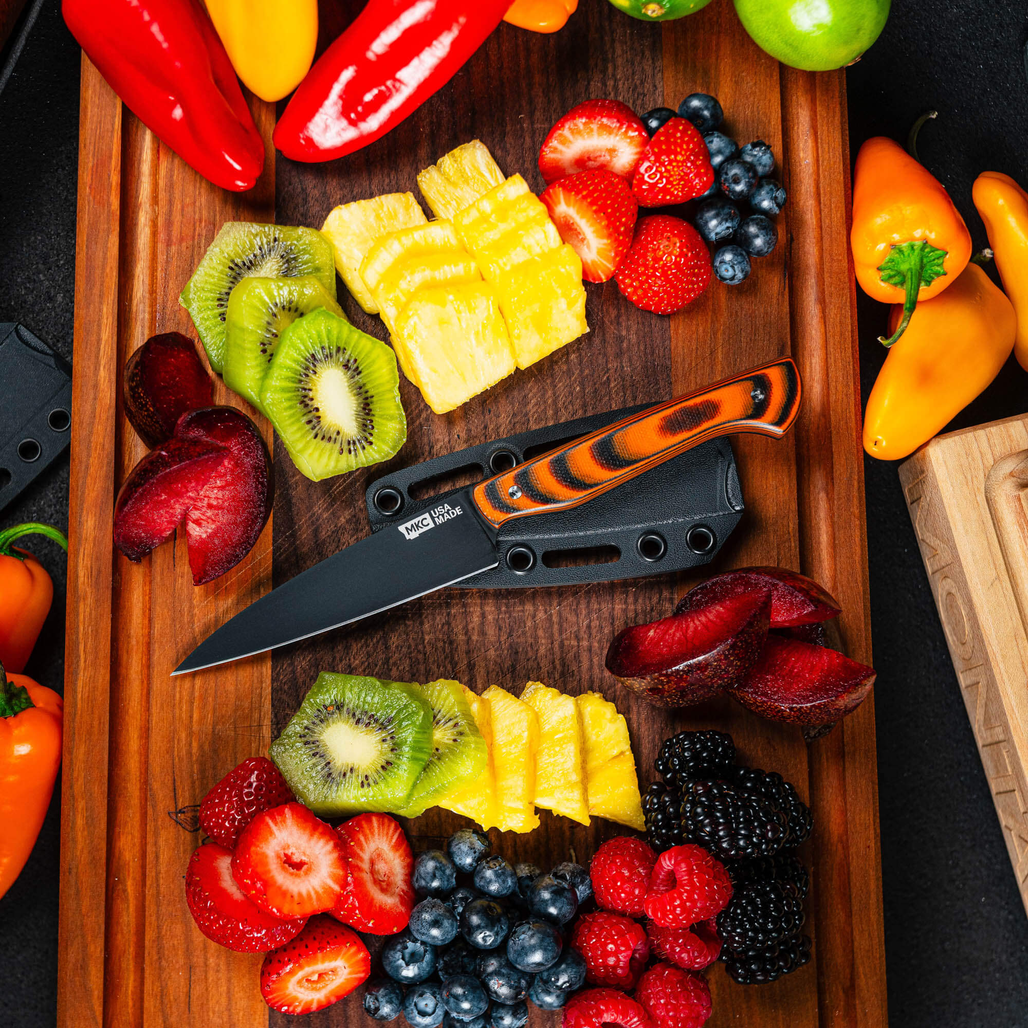 Montana Knife Company's Cutbank Paring Knife in orange and black, surrounded by vibrant fruits on a wooden cutting board.