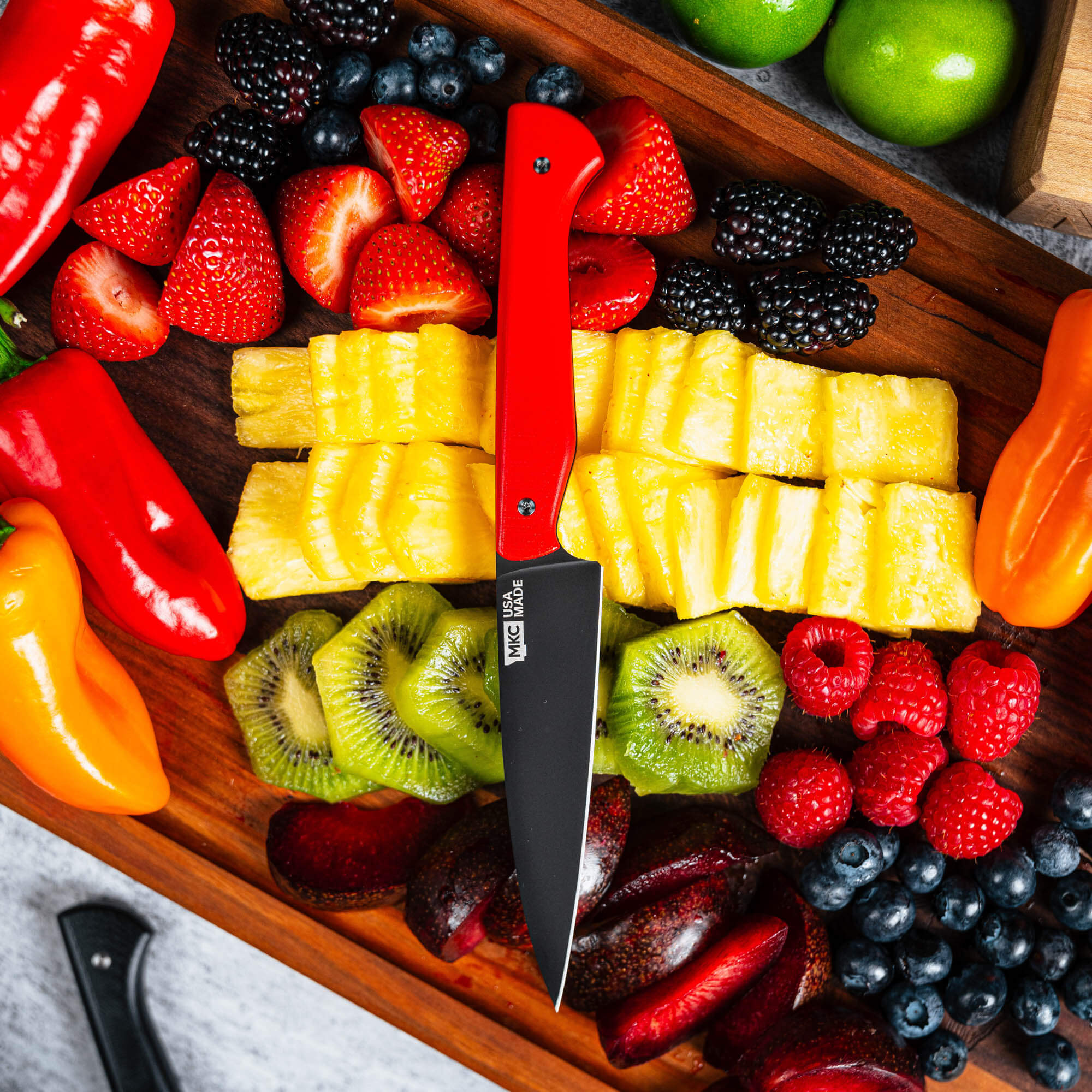 Red Cutbank paring knife on a wooden cutting board surrounded by vibrant fruits and vegetables, showcasing its sharp design.