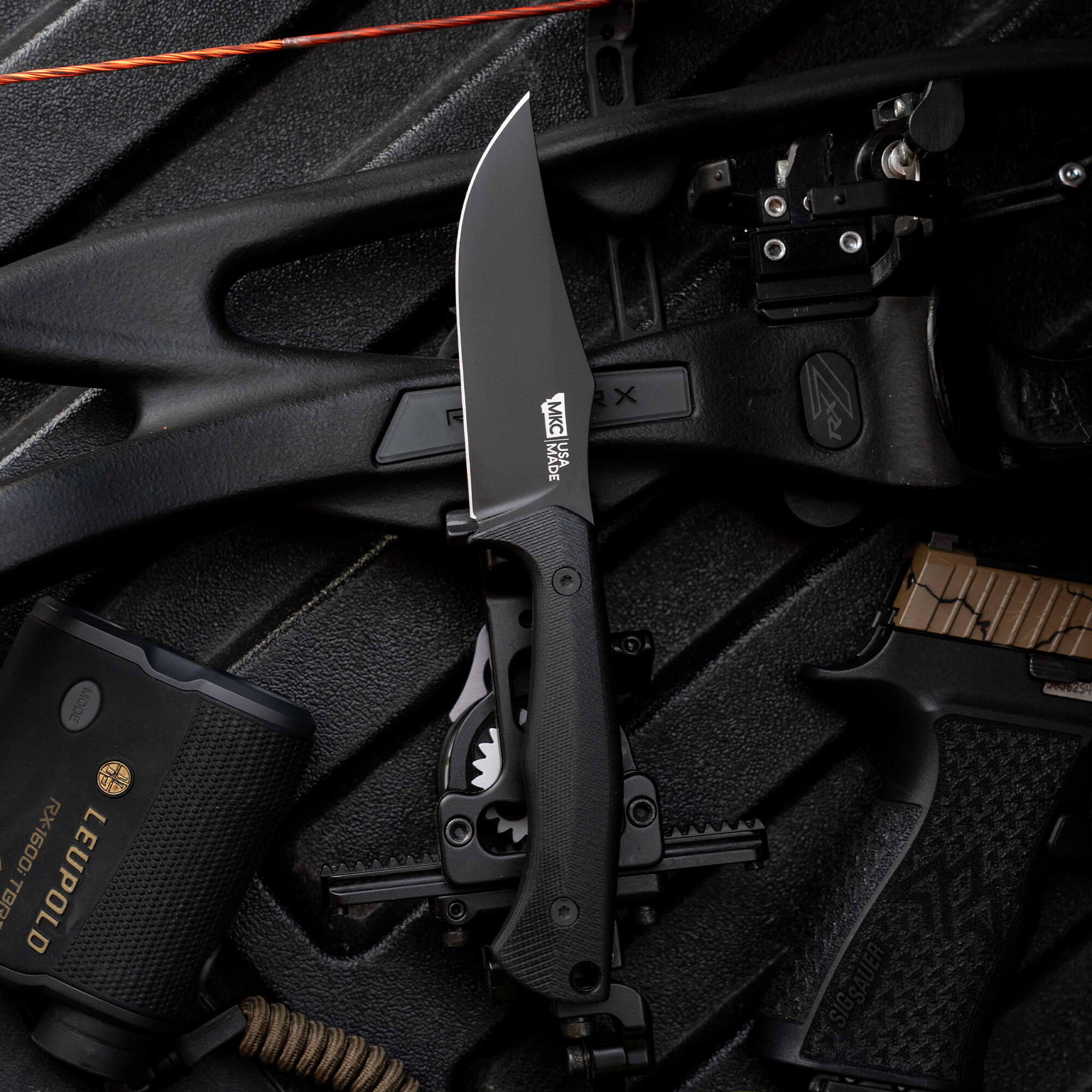 Montana Knife Company's Nock On Triumph Pro knife with a sleek black blade, surrounded by tactical gear and accessories.