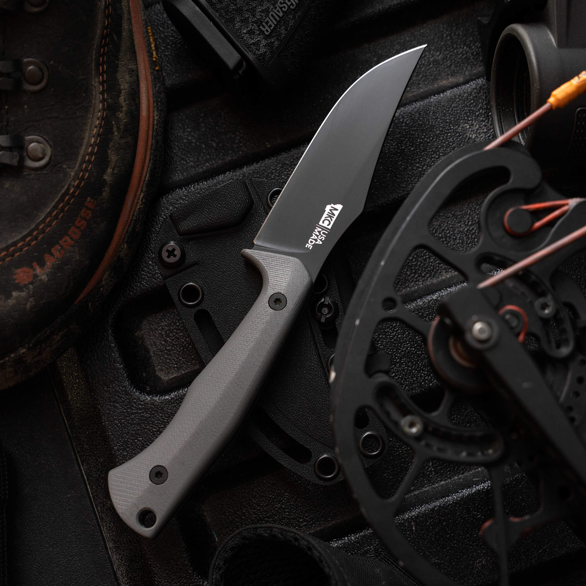 Montana Knife Company's Nock On Triumph Pro knife displayed on a textured surface with outdoor gear, showcasing its sleek design.