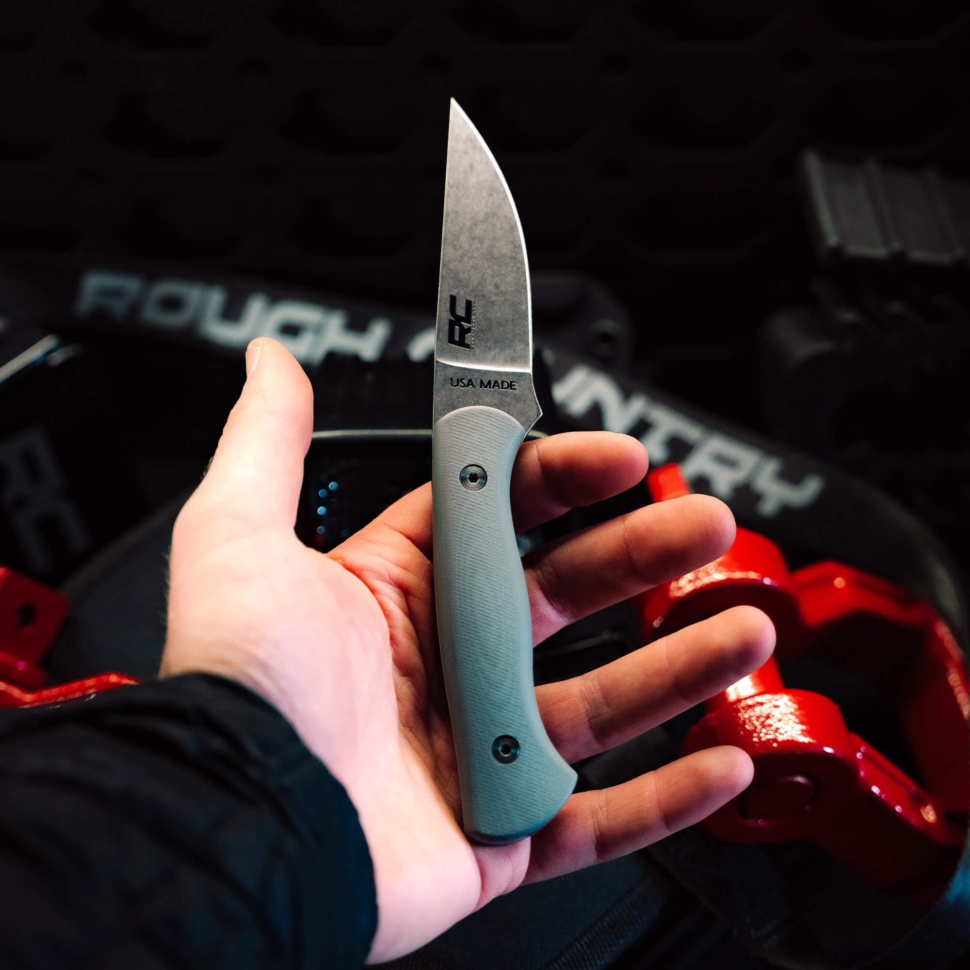 Hand holding the Rough Country Magnacut Blackfoot 2.0 knife with a gray handle, showcasing its American-made craftsmanship.