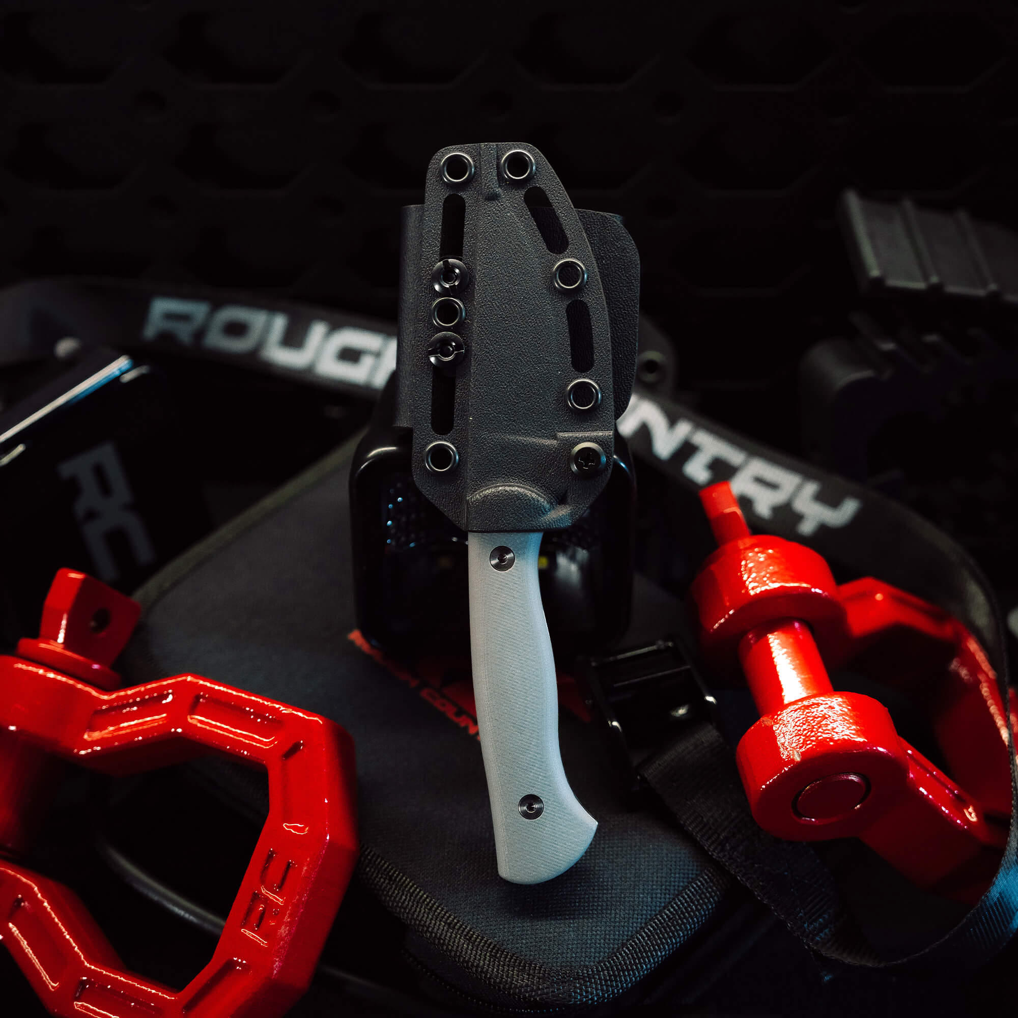 Rough Country Magnacut Blackfoot 2.0 knife in a sleek sheath, surrounded by red weights and workout gear.