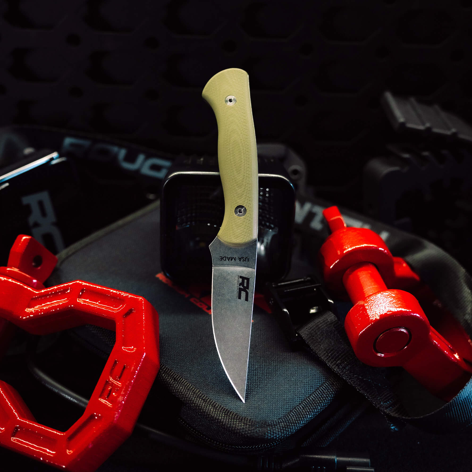Rough Country Magnacut Blackfoot 2.0 knife with a tan handle, displayed among red gear and tools, highlighting its rugged design.