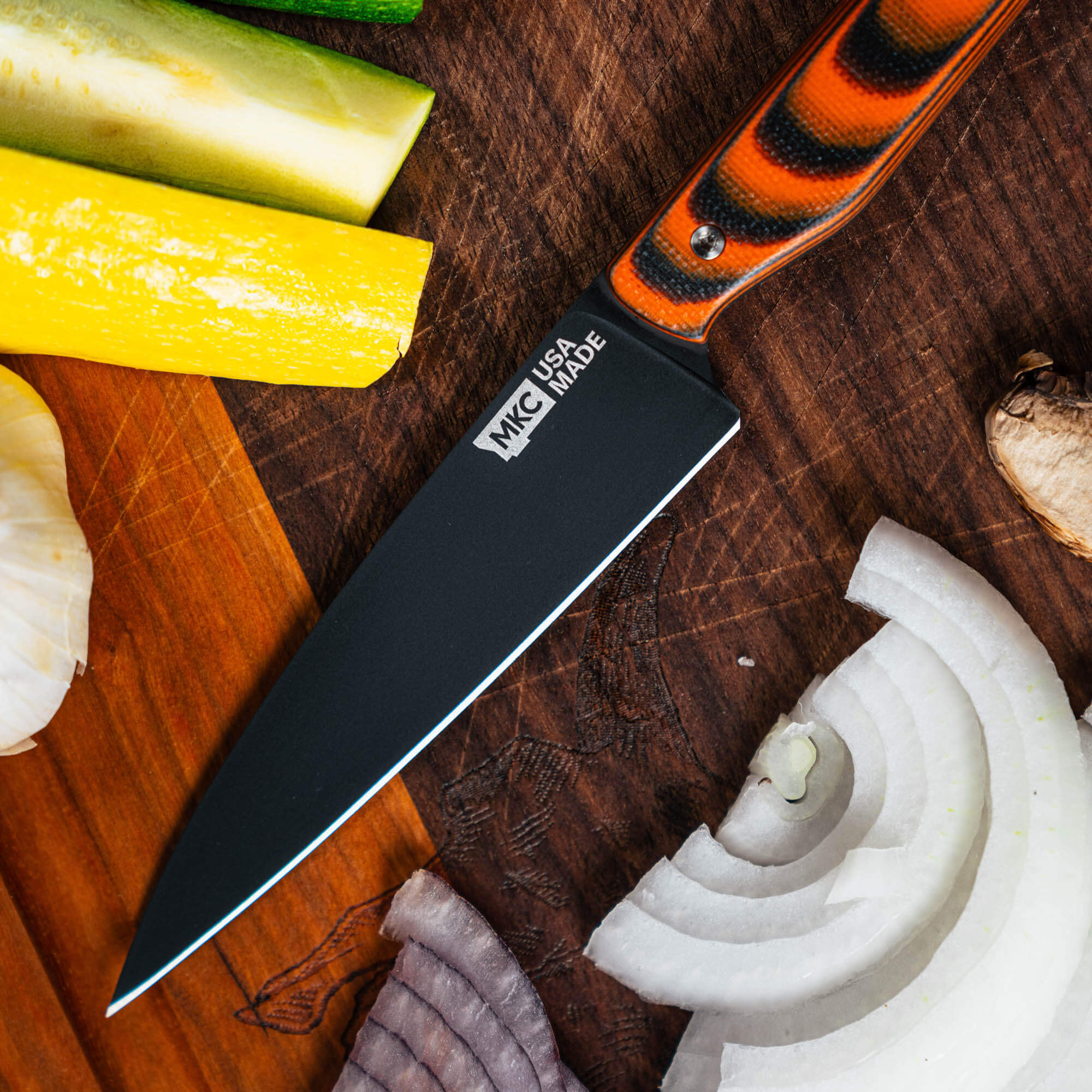 Montana Knife Company's Cutbank Paring Knife in orange and black, displayed with fresh vegetables on a wooden cutting board.