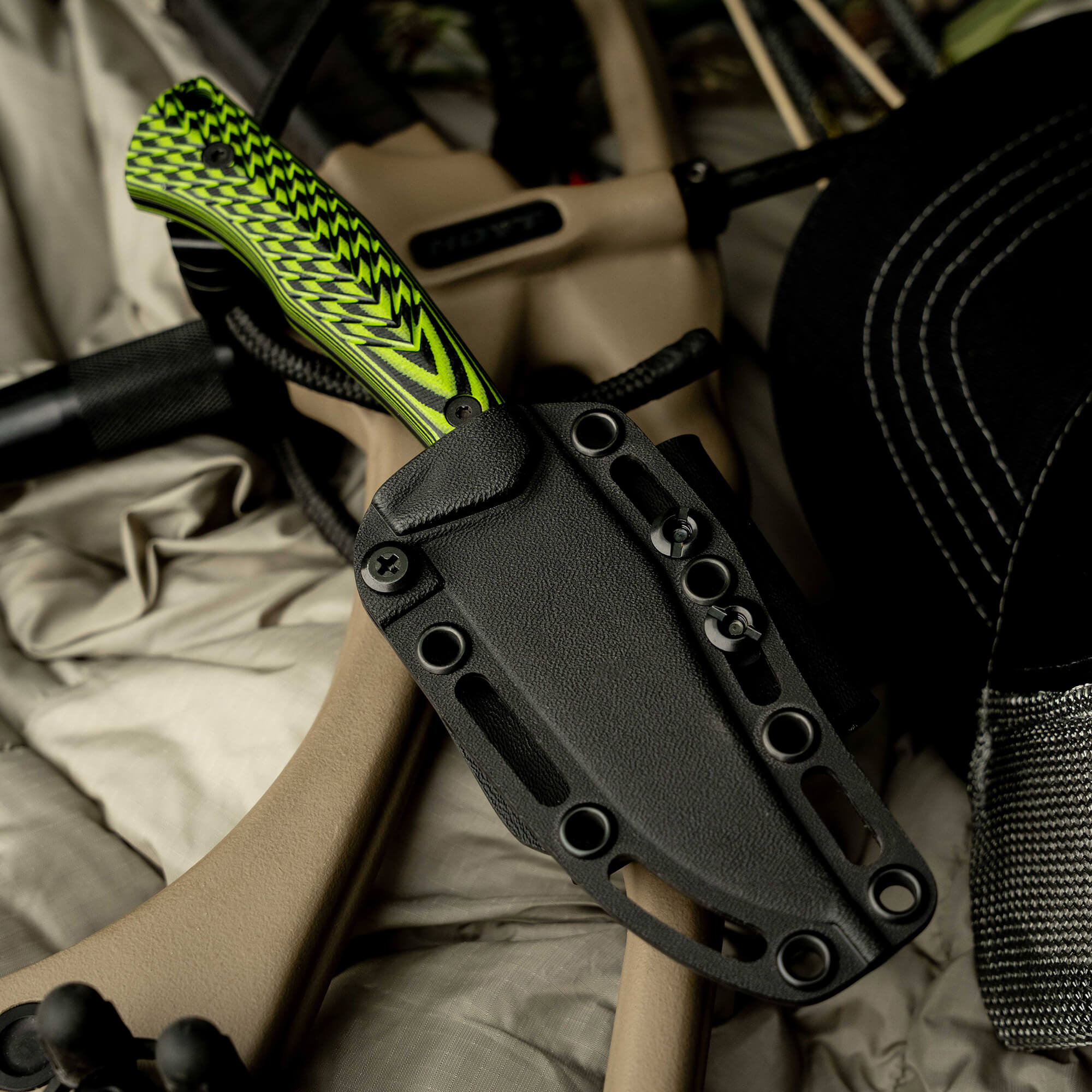 Nock On Triumph Pro knife in a black sheath, featuring a vibrant green handle, resting on outdoor gear.