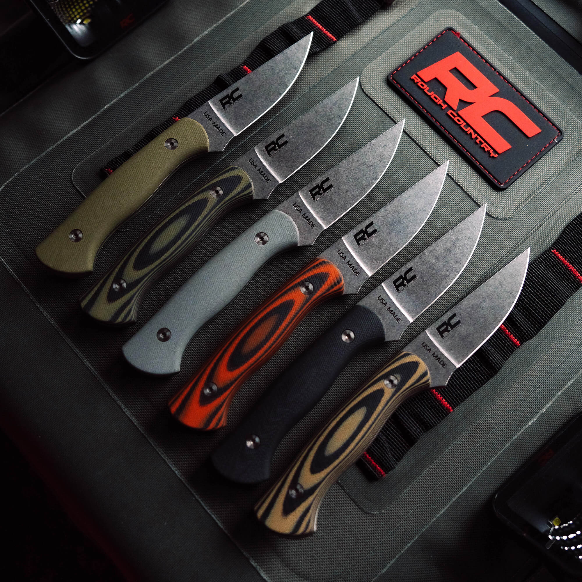 A collection of Rough Country Magnacut Blackfoot 2.0 knives featuring various handle colors and textures, displayed on a tactical background.