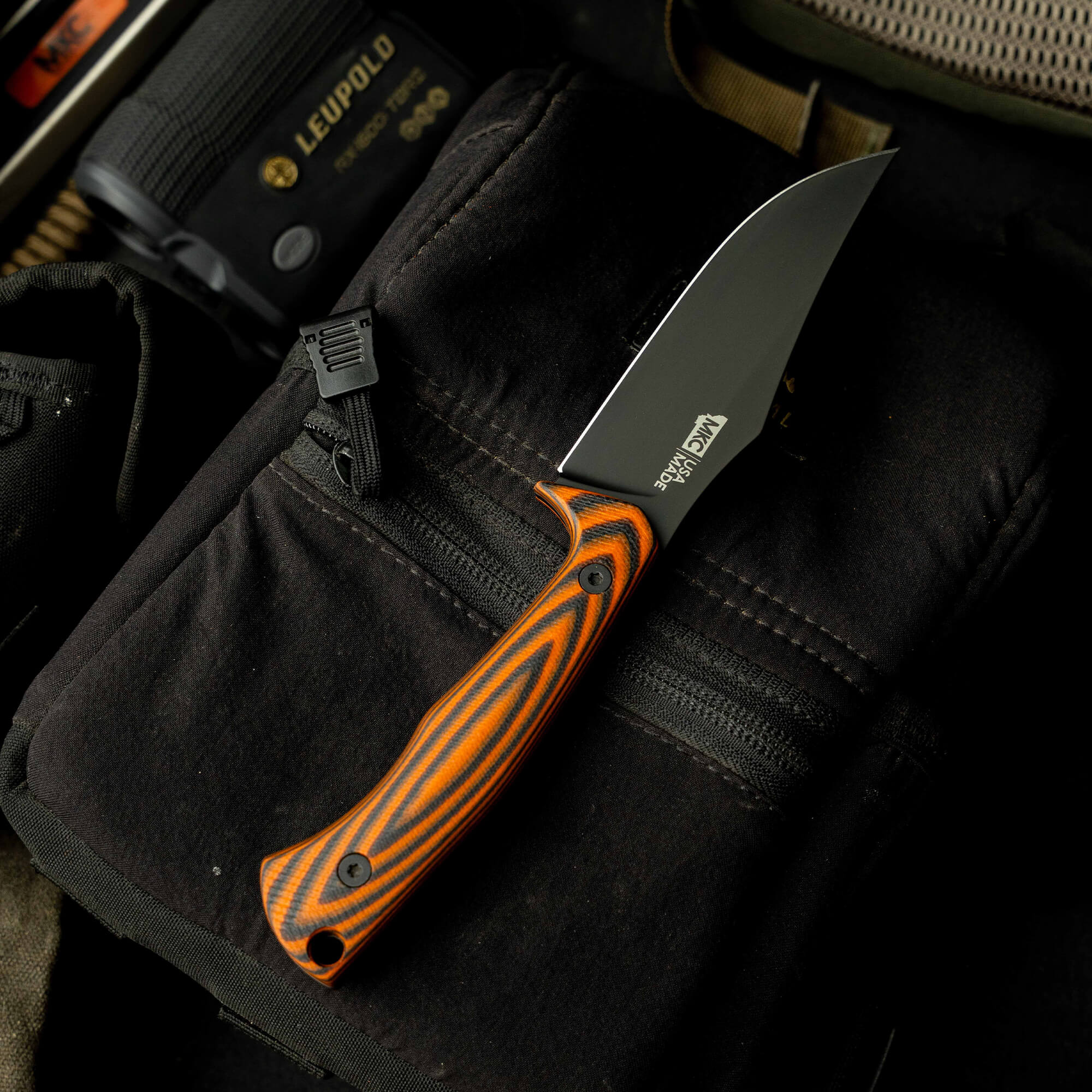 Nock On Triumph Pro knife with a black blade and orange striped handle, resting on a dark fabric background.